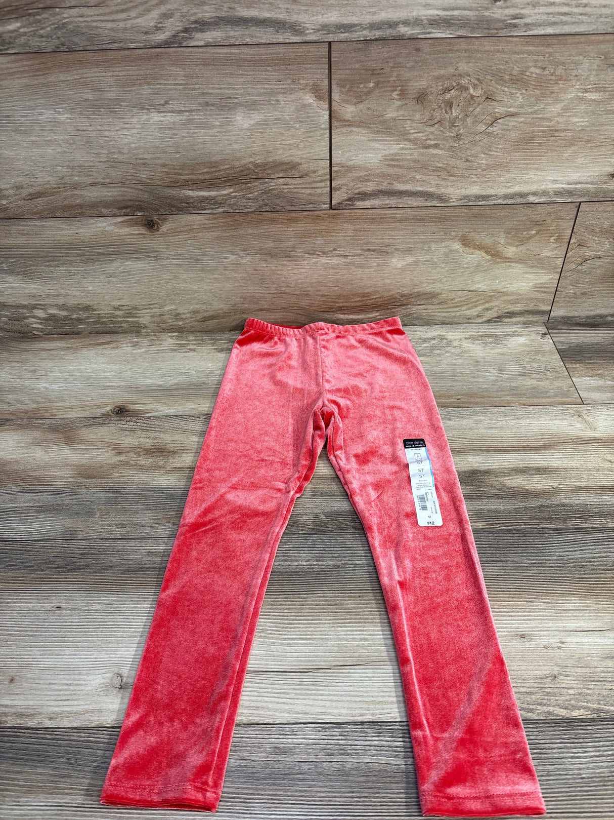 Pink velvet kids leggings with tag displayed on wooden floor