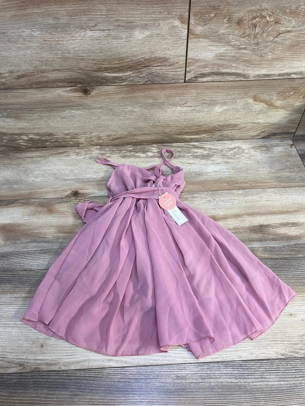 Flat-lay of pink sleeveless Bailey’s Blossoms baby dress 3-6 months showcasing gathered waist with tie and flowy skirt on light wood background
