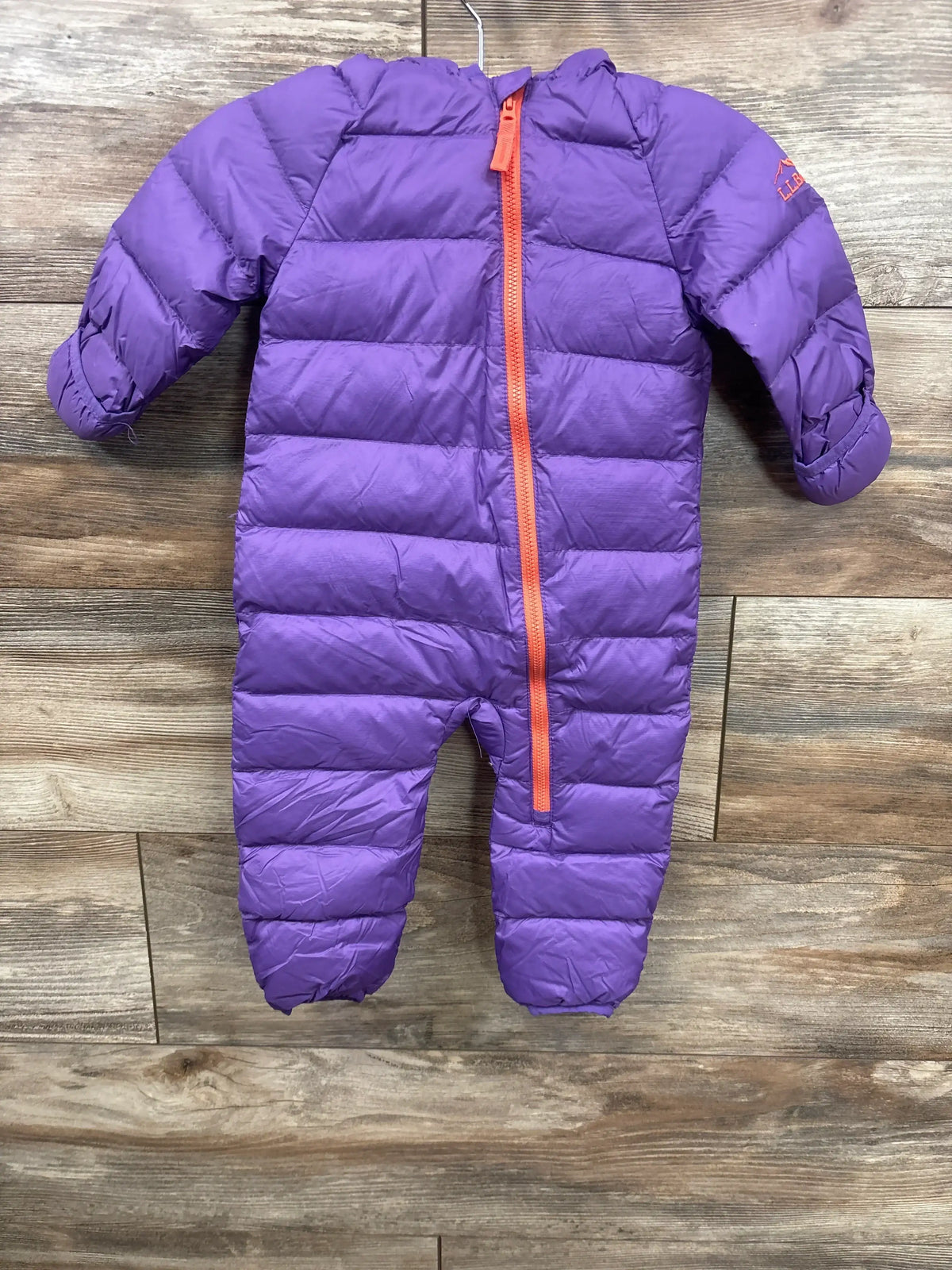 Purple puffer infant one-piece snowsuit with orange zipper hanging on wooden background