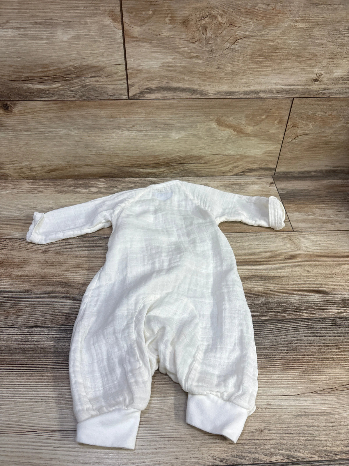 Top view of Under The Nile Organic Muslin Kimono Coverall in ivory, showing long sleeves and foot cuffs on wood floor