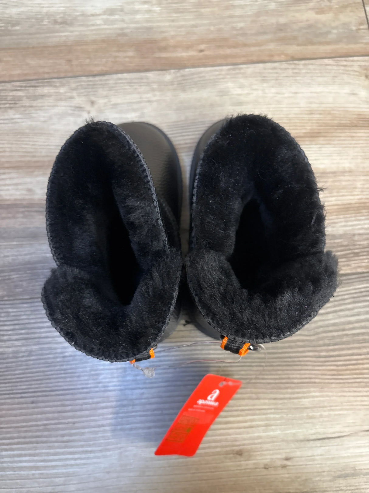 Black faux fur lined toddler boots with orange stitching on wooden floor
