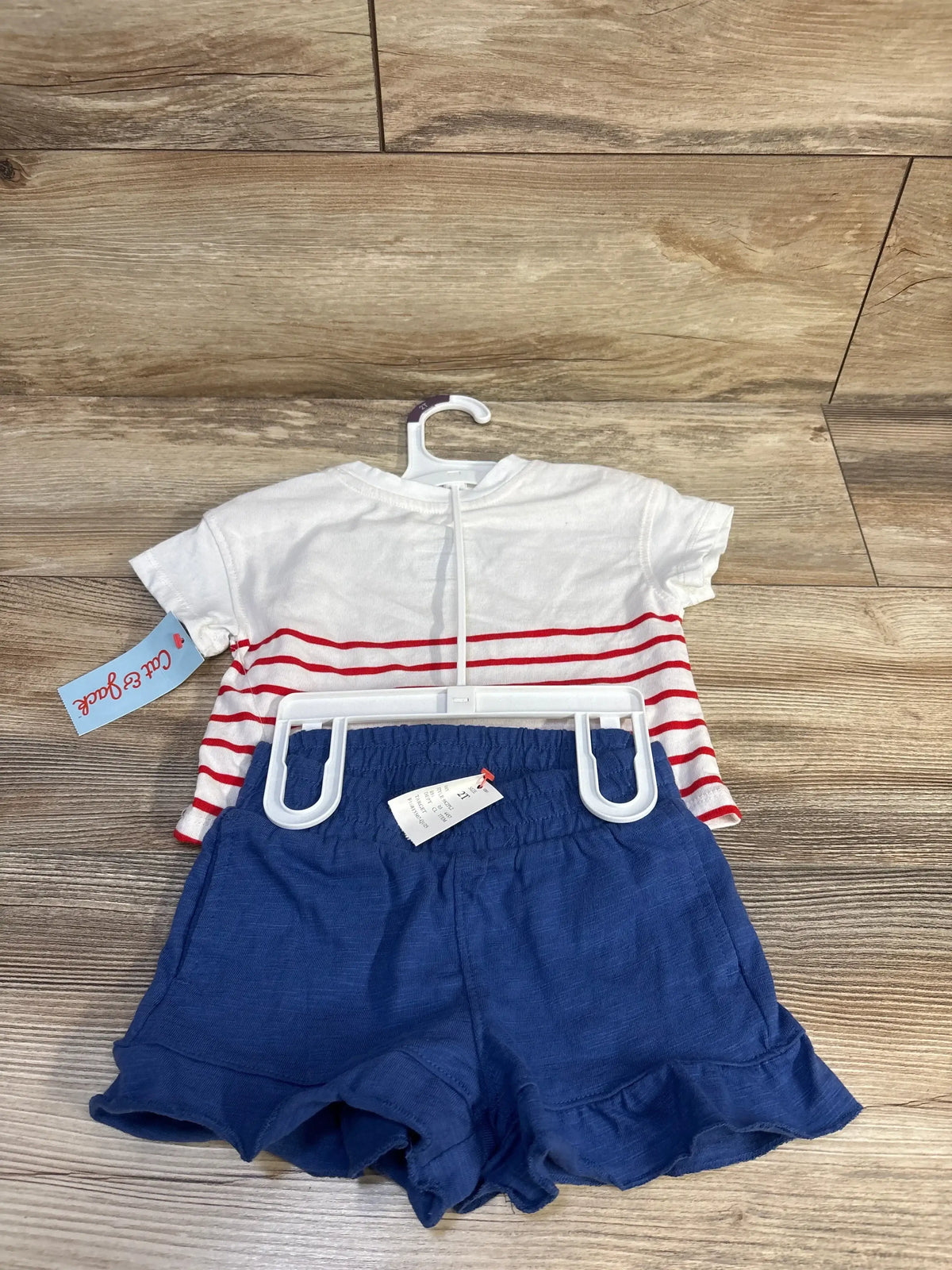 Back view of Cat & Jack toddler two-piece Fourth of July set with white tee featuring red stripes and navy ruffle shorts on wood floor
