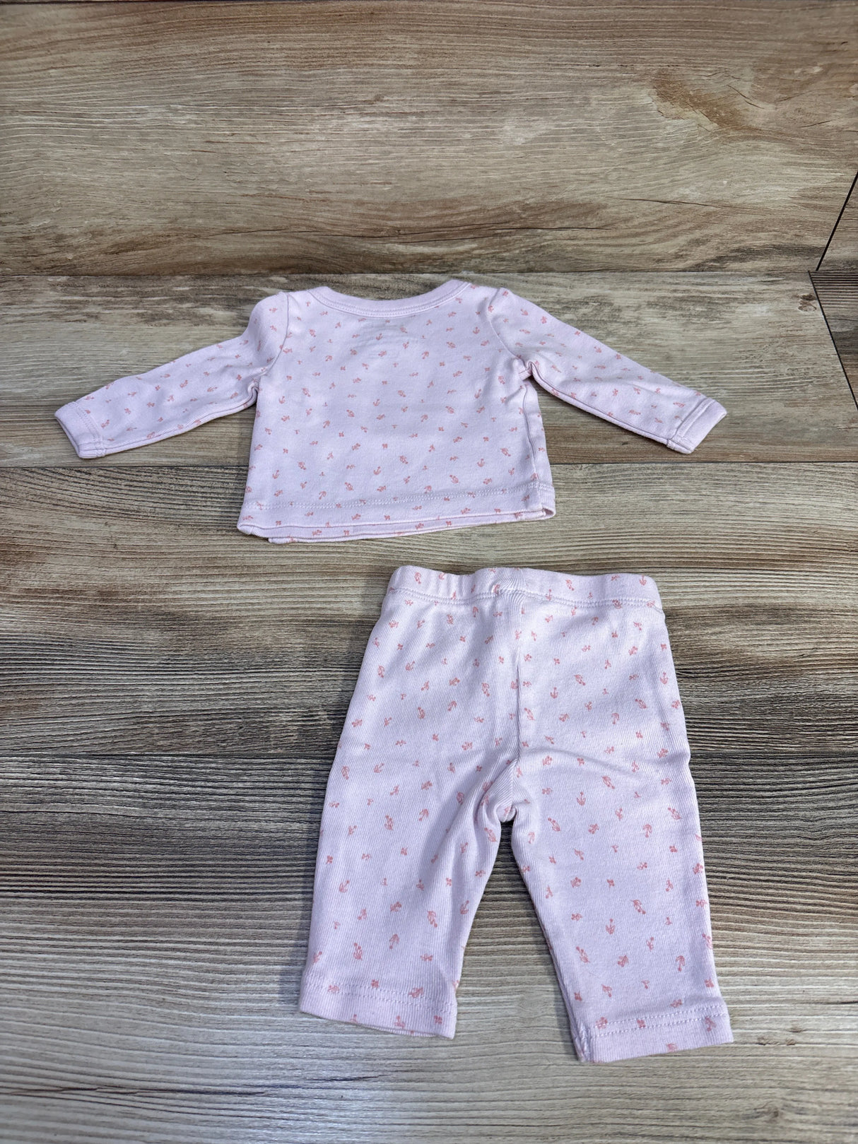 Light pink baby outfit with long sleeve shirt and pants, small pink pattern, wood background