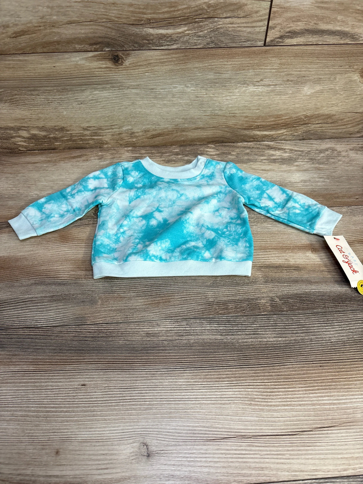 Flat-lay of Cat and Jack blue tie-dye newborn sweatshirt with shoulder snap, long sleeves and ribbed cuffs on wood background