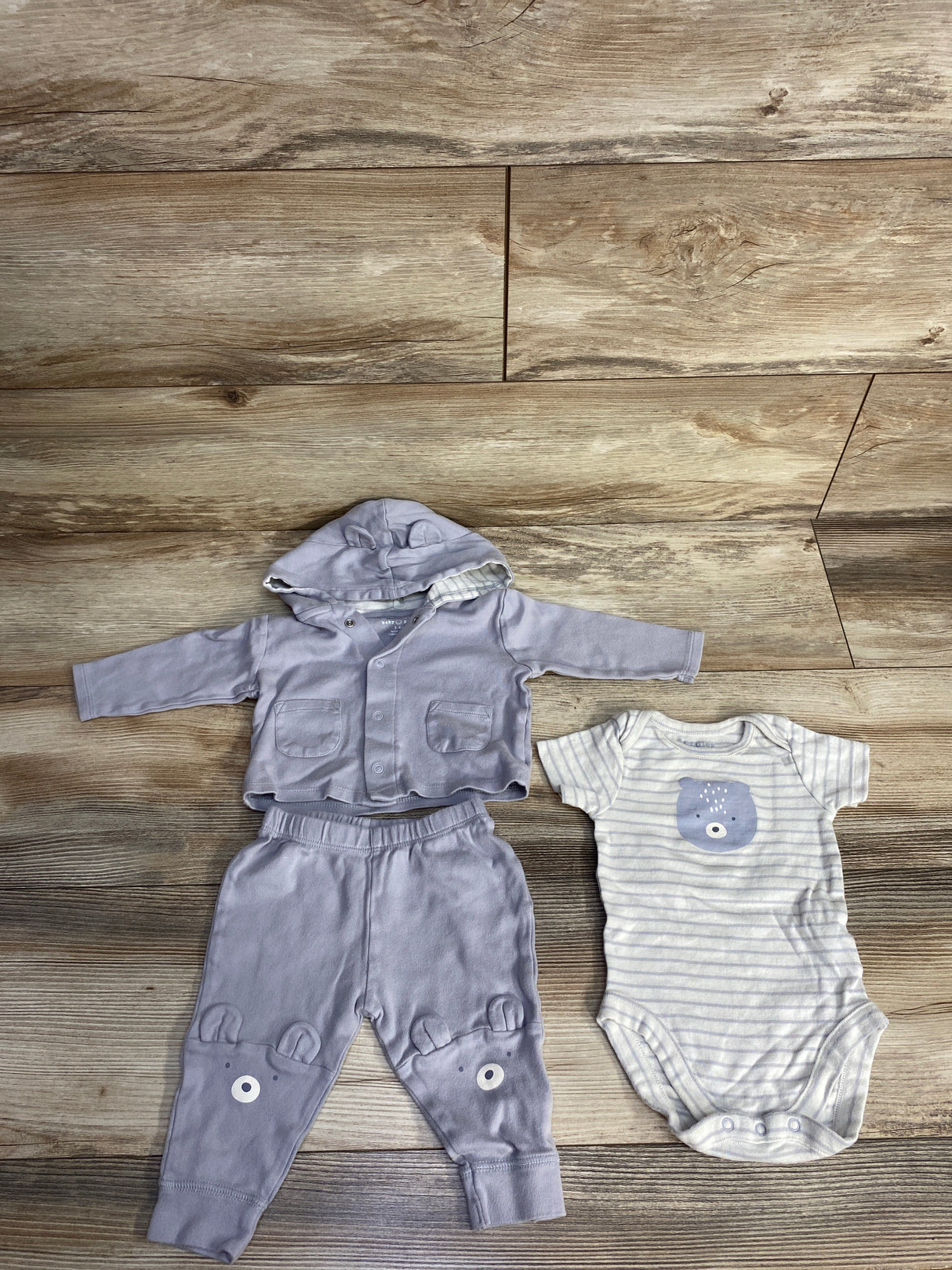 Light purple baby hoodie and pants with bear faces, white striped baby onesie with bear graphic on wooden floor