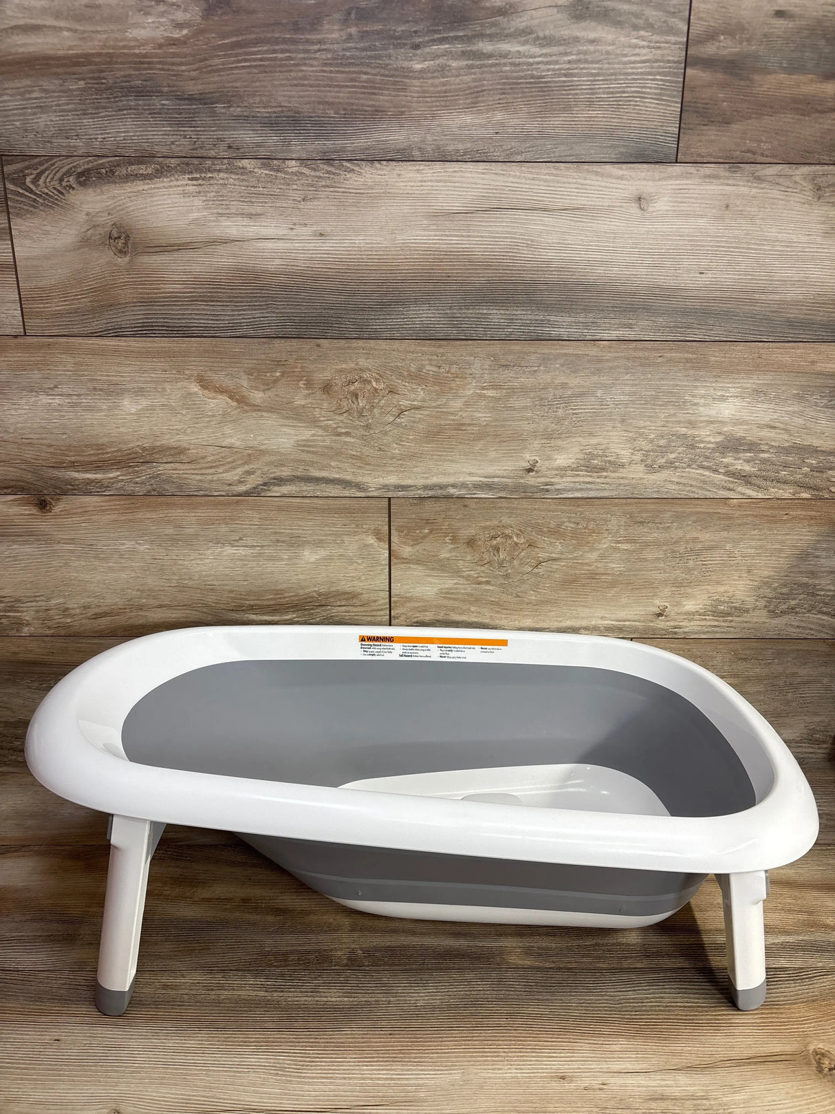 Side view of OXO Tot Splash & Store bathtub showing gray collapsible basin and fold-out legs on wood floor