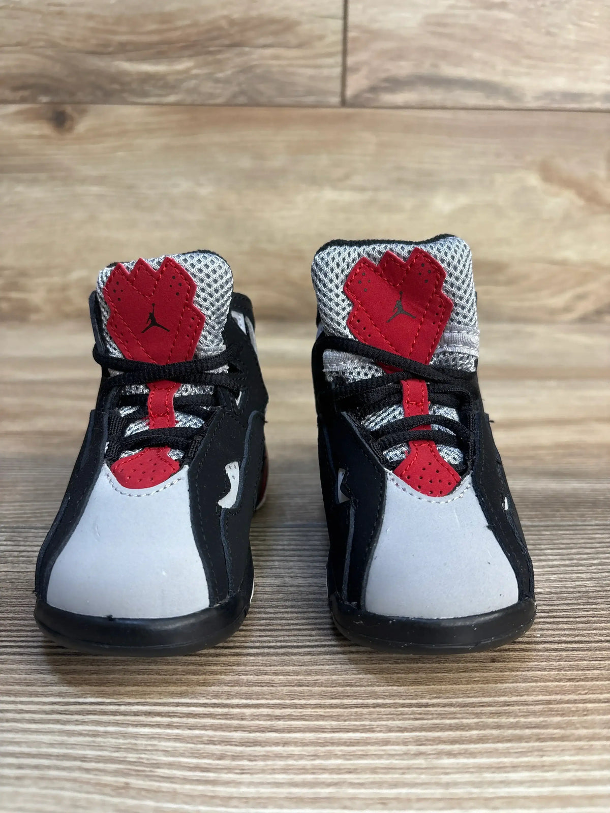 Front view of Air Jordan True Flight TD toddler sneakers in black, red and grey showing mesh tongues, Jumpman logo, and padded ankle on wood floor