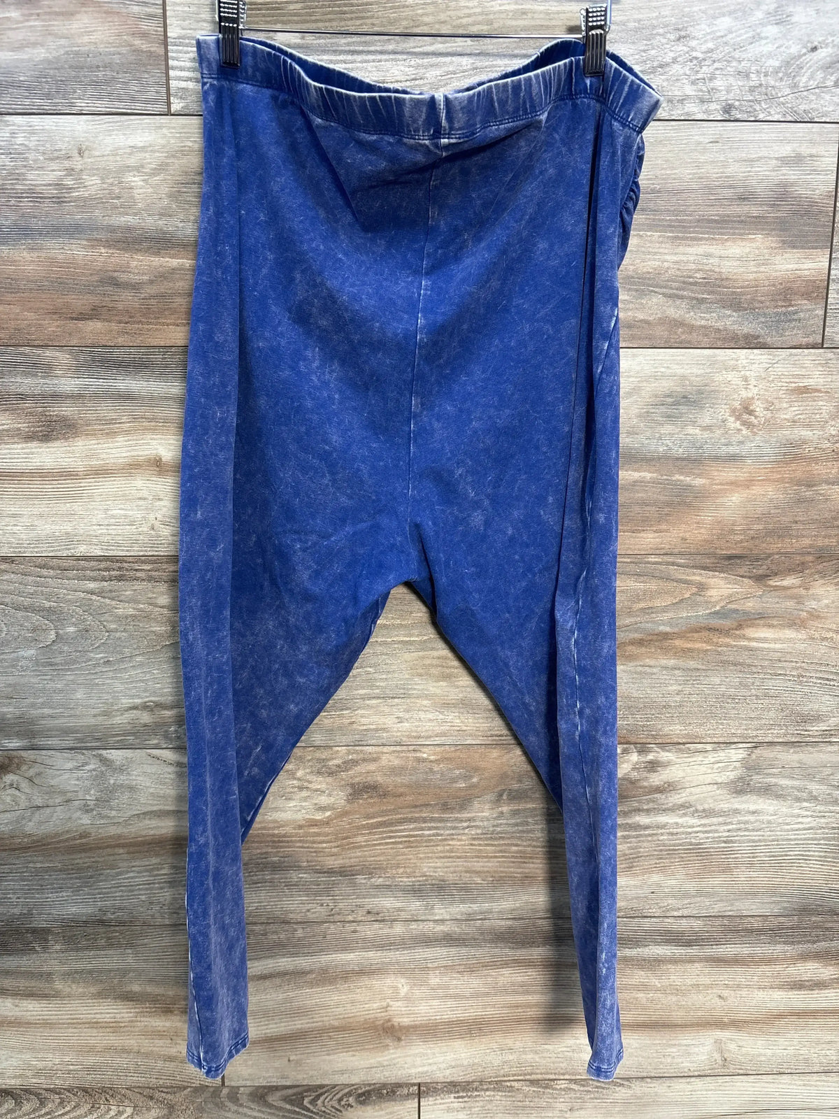 Blue acid wash drop-crotch pants hanging on wood panel background