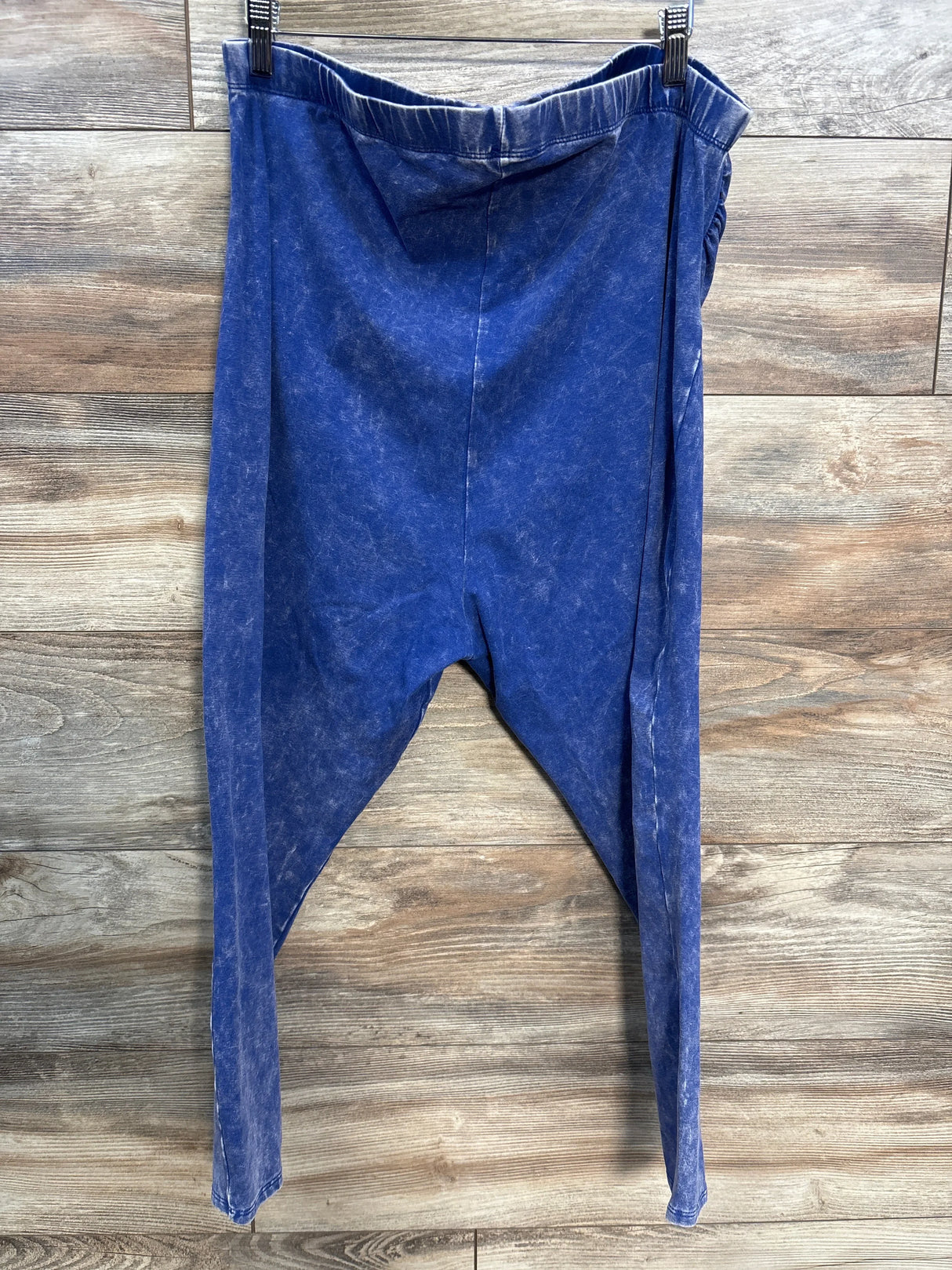 Blue acid wash drop-crotch pants hanging on wood panel background