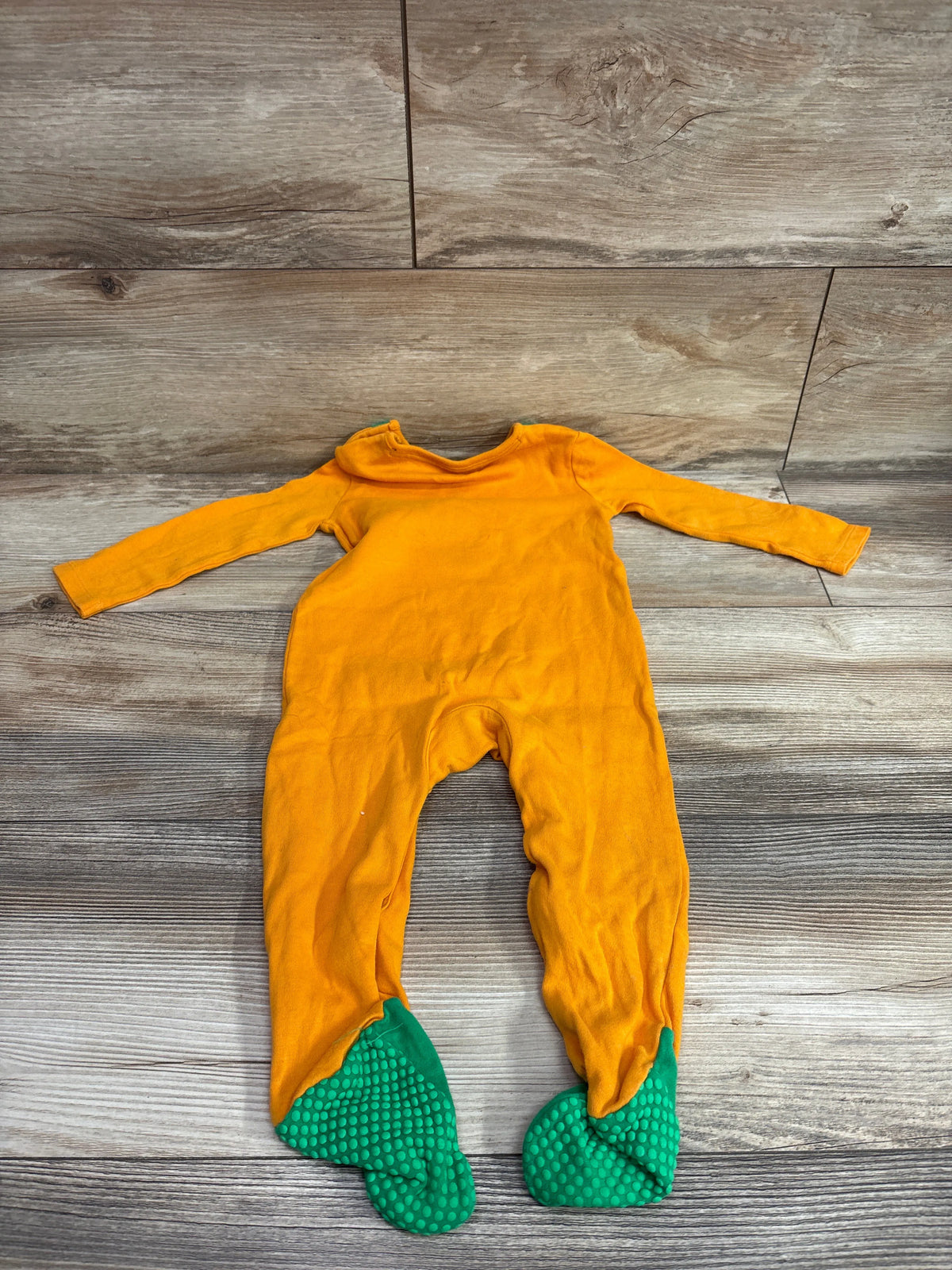 Front view of Fred and Flo Cutest Pumpkin footie showcasing orange long sleeves and green textured foot coverings on a wood floor