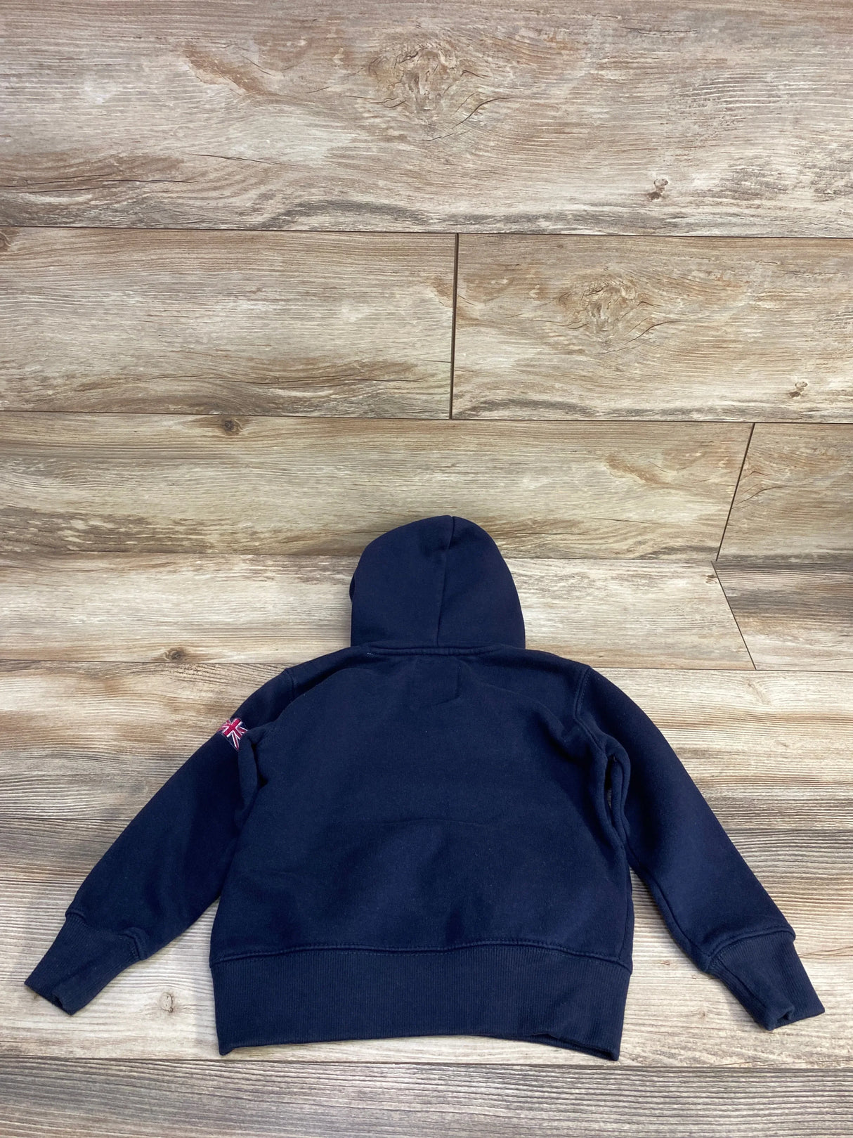 Navy blue kids hoodie with Union Jack patch on sleeve, laid flat on wood floor