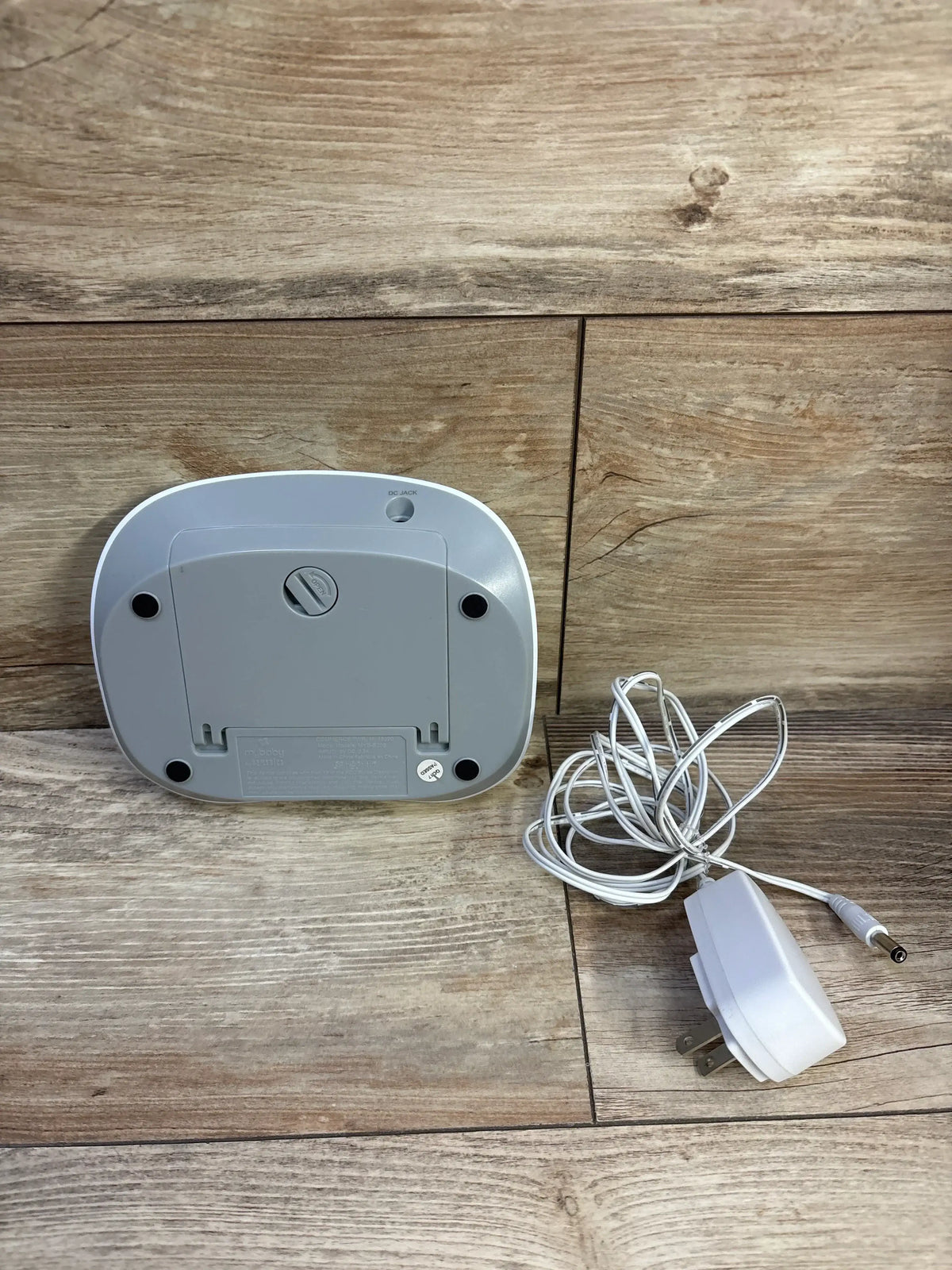 Back view of Homedics MyBaby SoundSpa Portable Sound Machine in white with included power adapter on a wood plank background