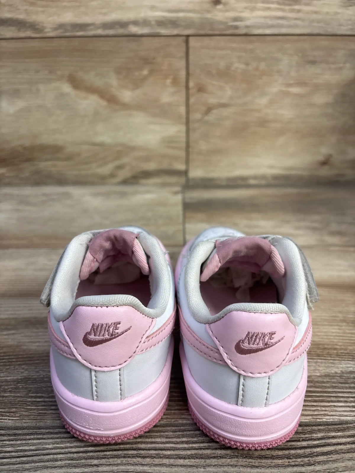 Rear view of toddler Nike Air Force 1 Low EasyOn sneakers in white and pink showcasing heel logos and Velcro straps on wood floor