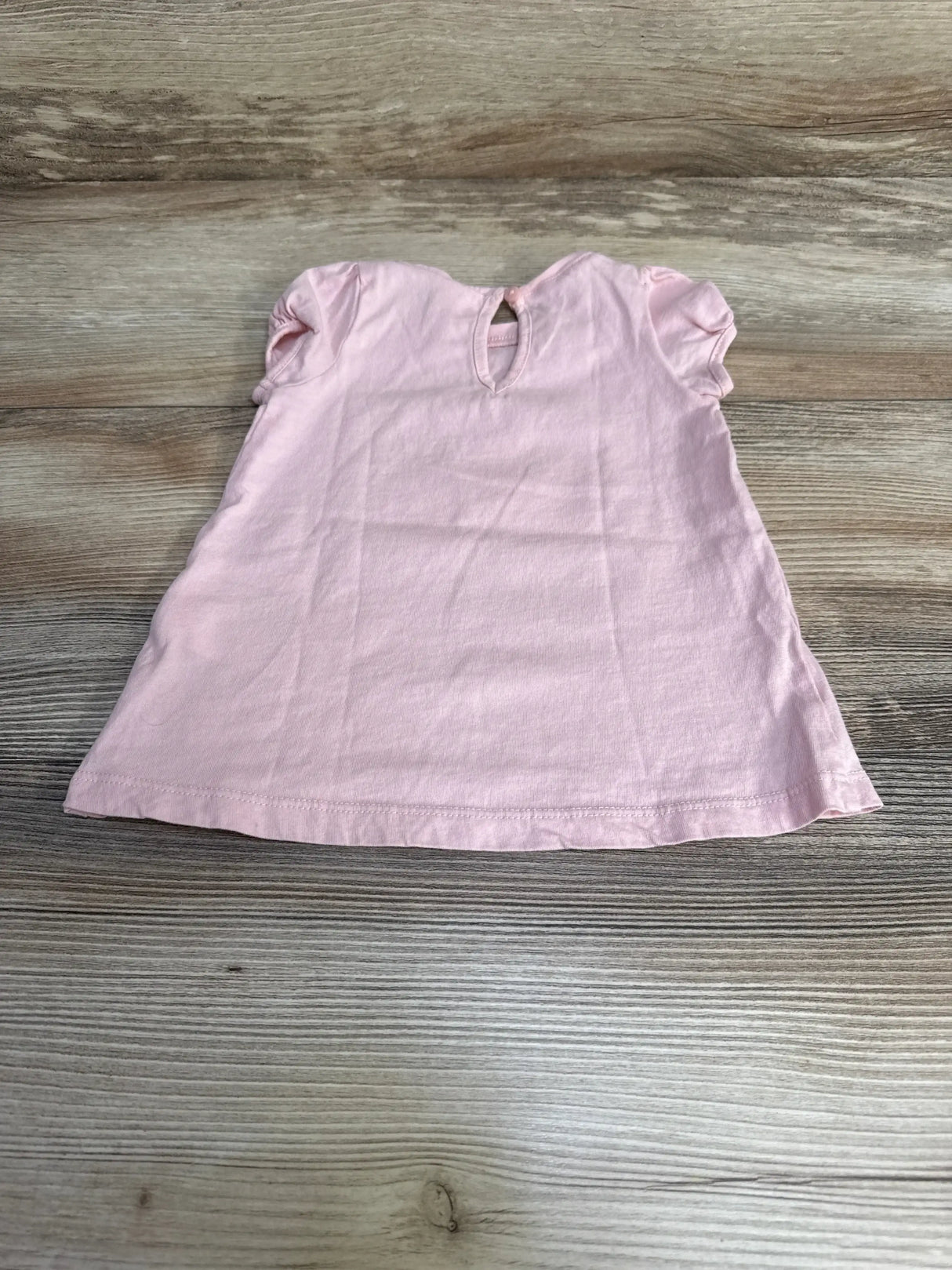 Flat lay of pink H&M baby shirt size 6 months showing puff sleeves, A-line shape, and back keyhole with button on light wood background