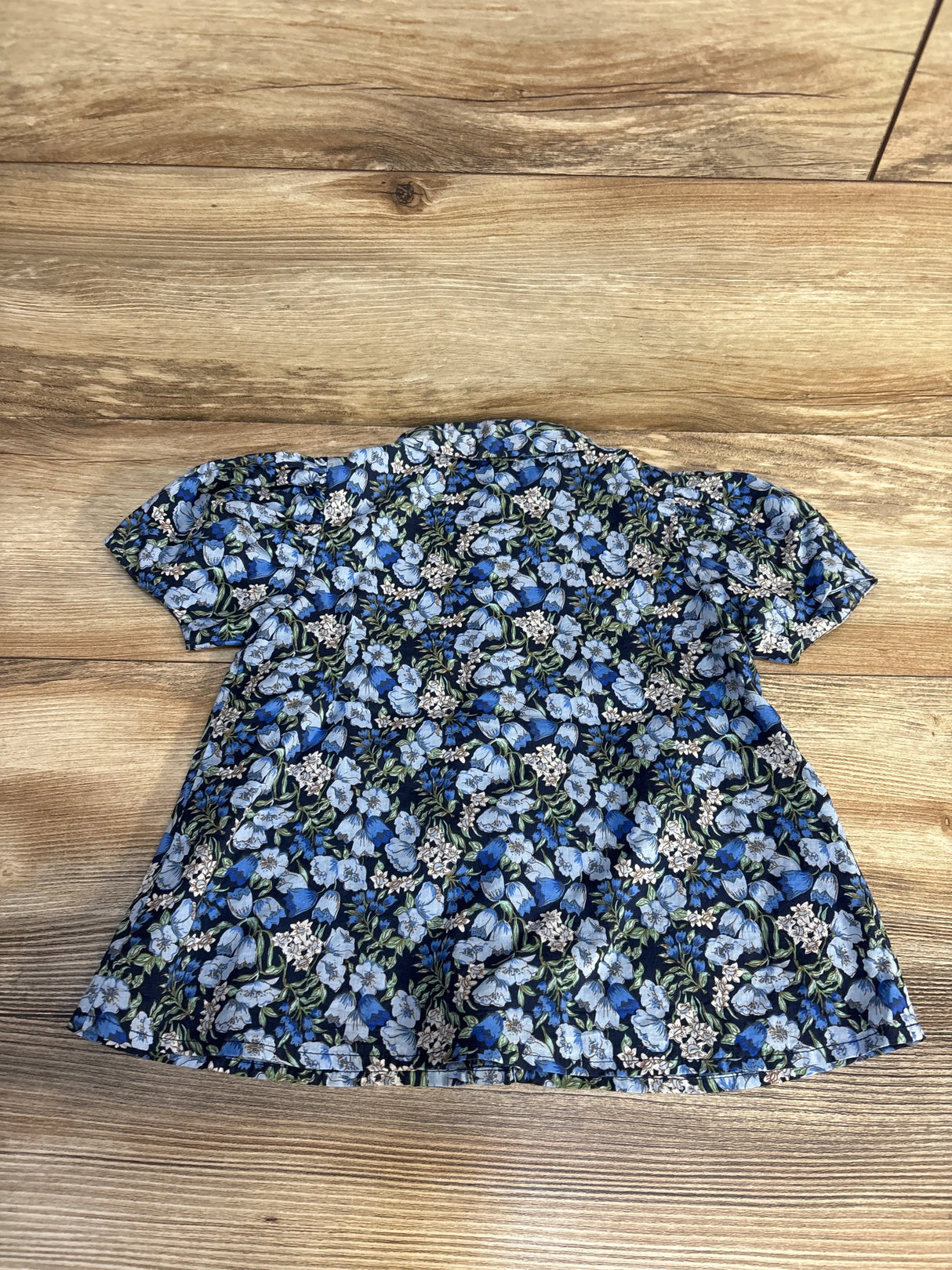 Top view of Janie and Jack floral puff sleeve button-up shirt showcasing blue pattern and short sleeves on a wood floor