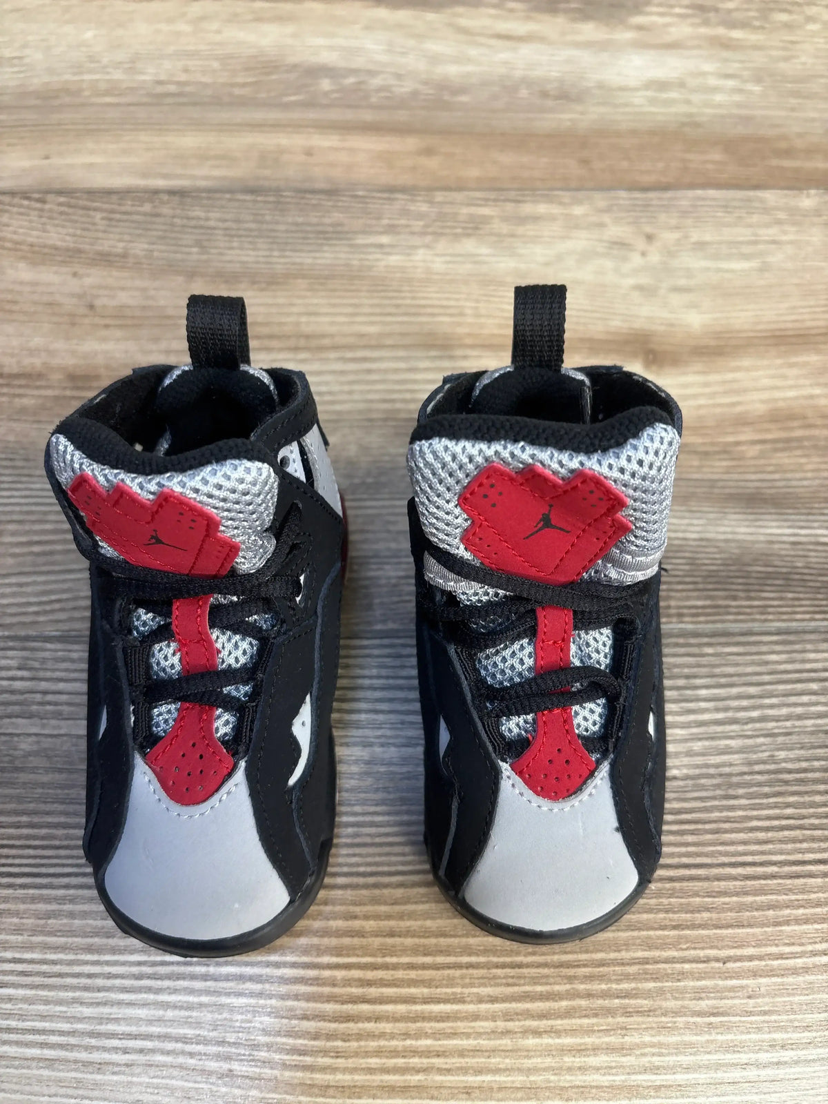 Top down view of Air Jordan True Flight TD sneakers in black grey and red with Jumpman logo on tongue and hook and loop strap on wood plank floor