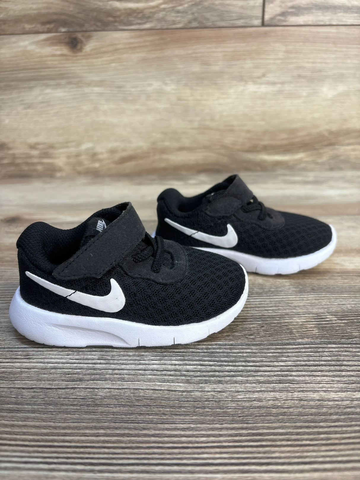 Black toddler sneakers with white soles and swoosh logo on wood background