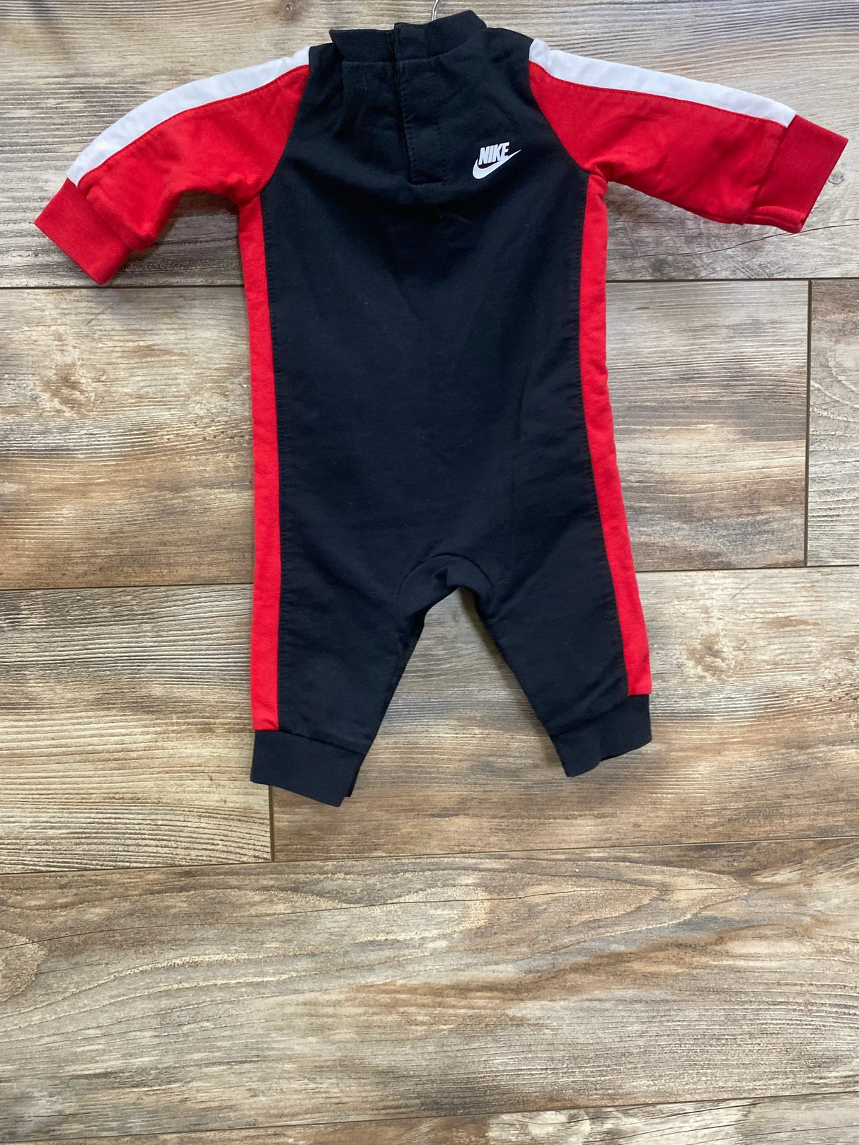 Black and red Nike baby romper with long sleeves and hood on wooden floor