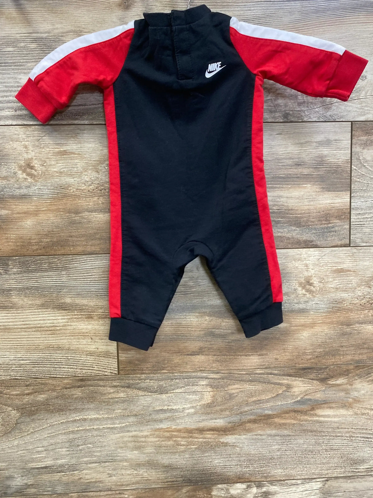 Black and red Nike baby romper with long sleeves and hood on wooden floor