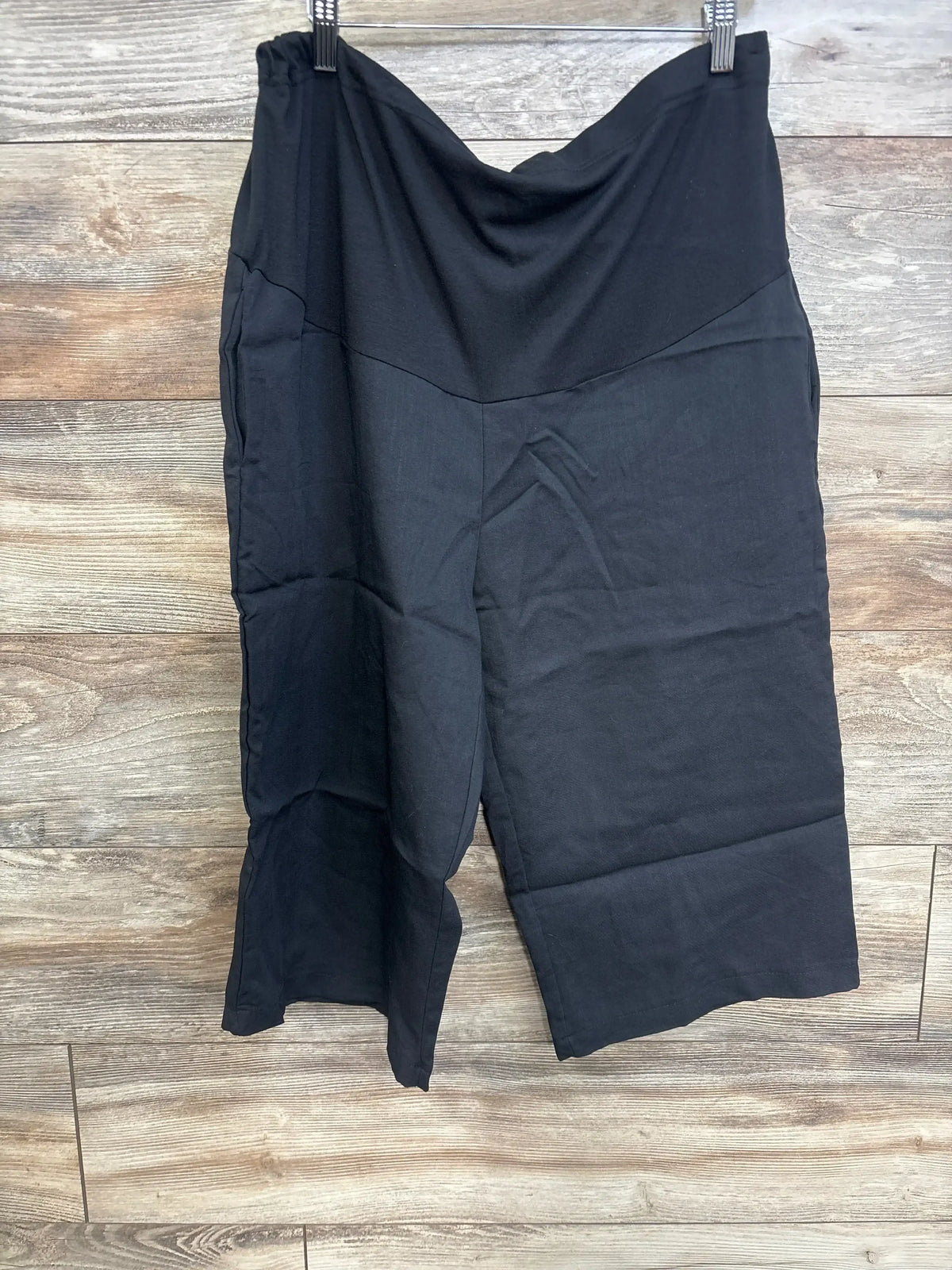 Front view of black knee-length maternity shorts showing V-front belly panel and elastic waistband on wood background