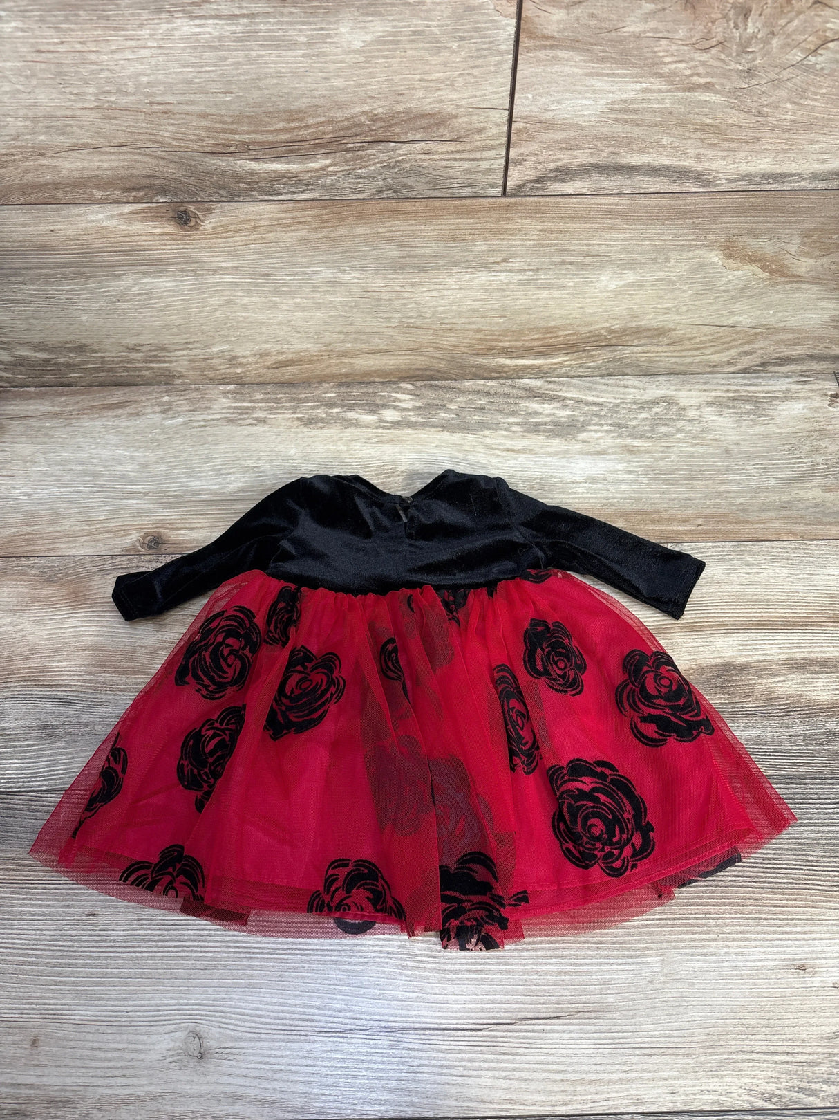 Baby girl's black velvet top dress with red tulle skirt featuring black floral patterns on wooden floor