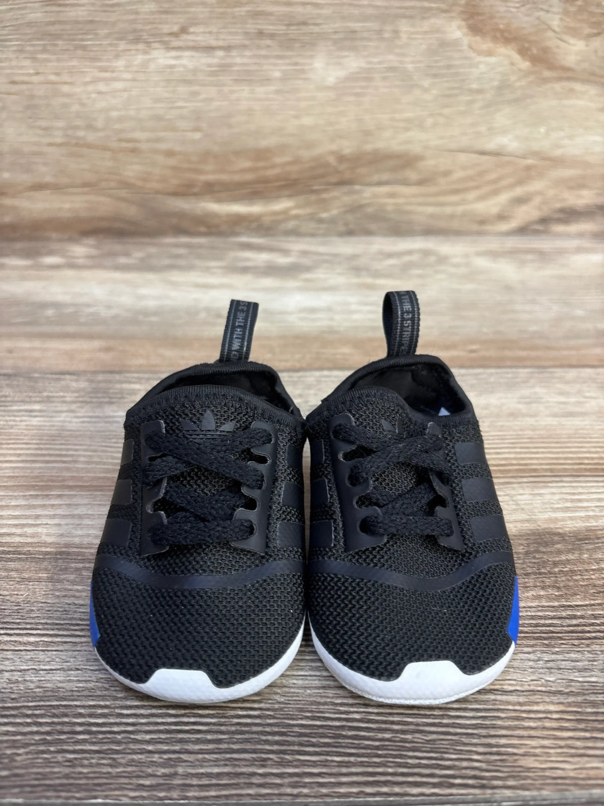 Front view of Adidas NMD soft sole sneakers in black, showcasing elastic lace closures and white outsoles on a wood surface