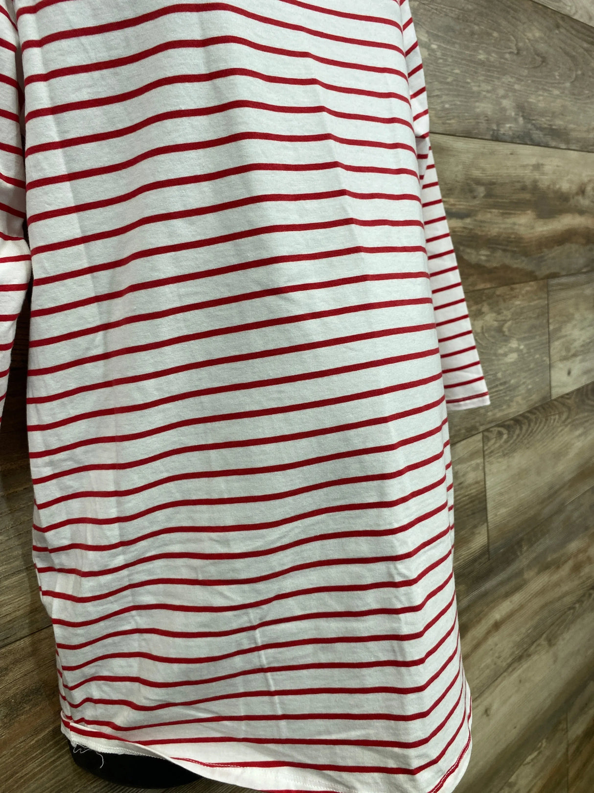 Close-up front view of maternity long-sleeve shirt showcasing white fabric with thin red horizontal stripes on wood background