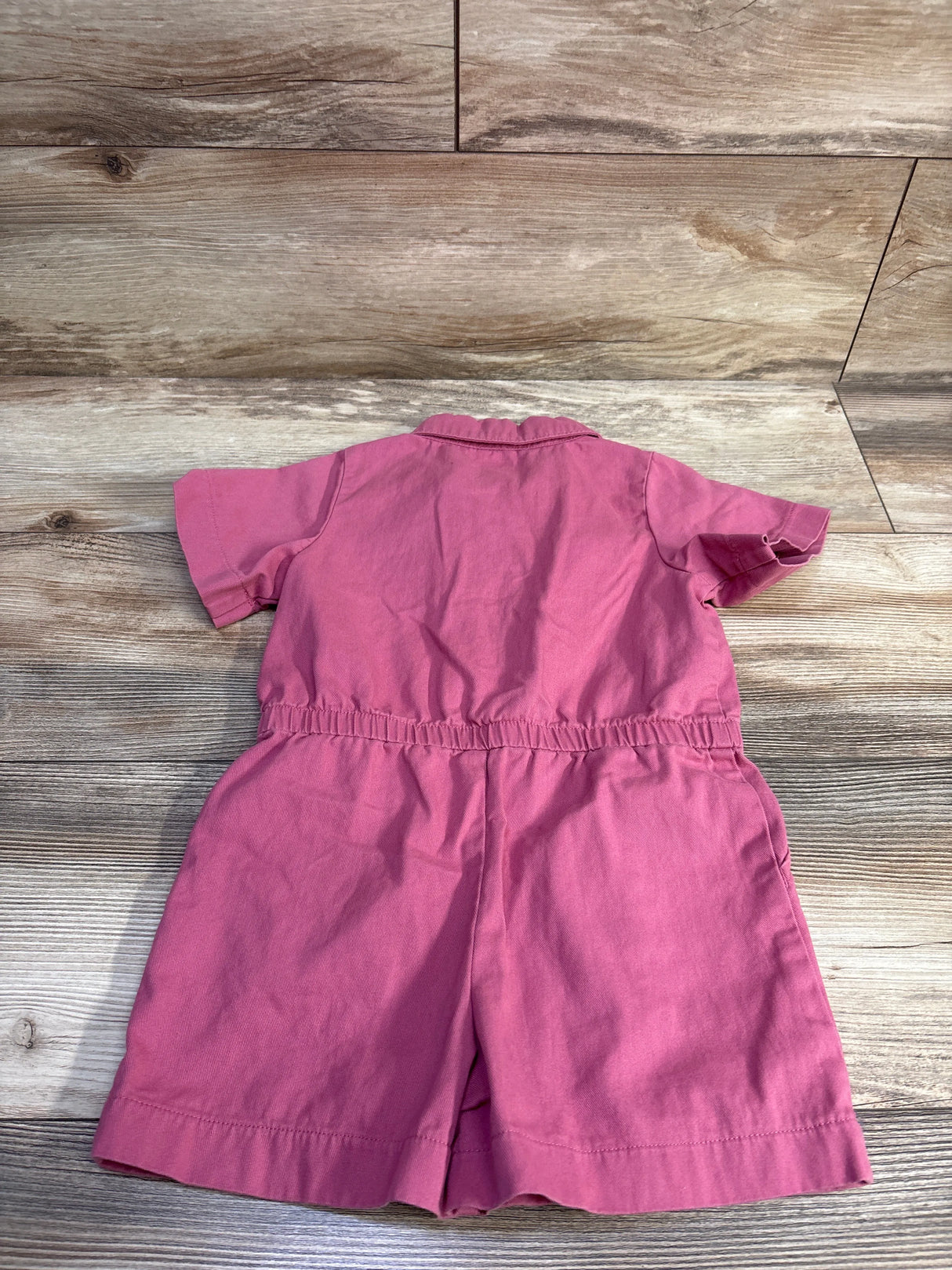 Back view of Oshkosh polo shortie romper in pink showcasing elastic waist, short sleeves, and collar on wooden floor