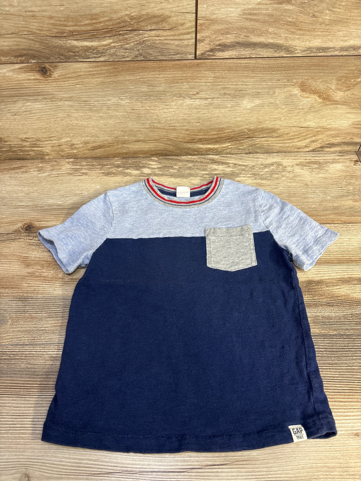 Kids color block t-shirt with heather gray top, navy bottom, gray chest pocket, and striped collar on wooden floor