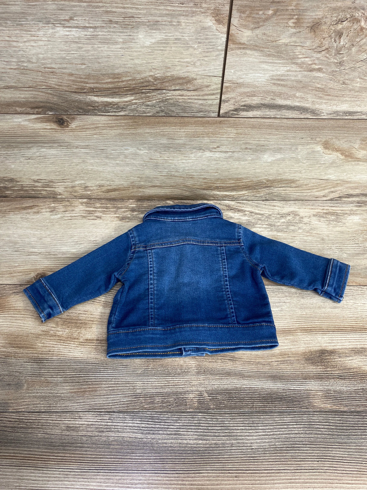 Back view of a toddler-sized blue denim jacket laid flat on wooden floor