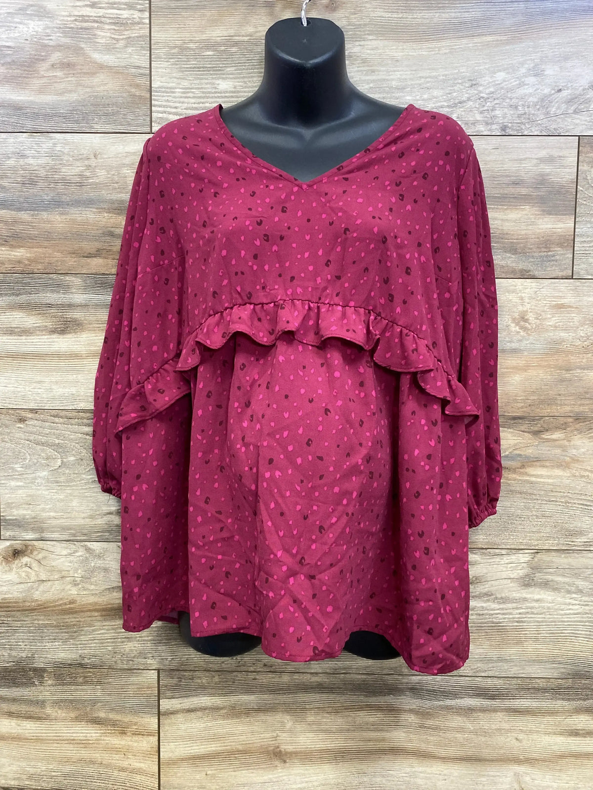 Front view of berry Isabel maternity ruffle-waist woven top showing ruffle over belly and small heart print on wooden background