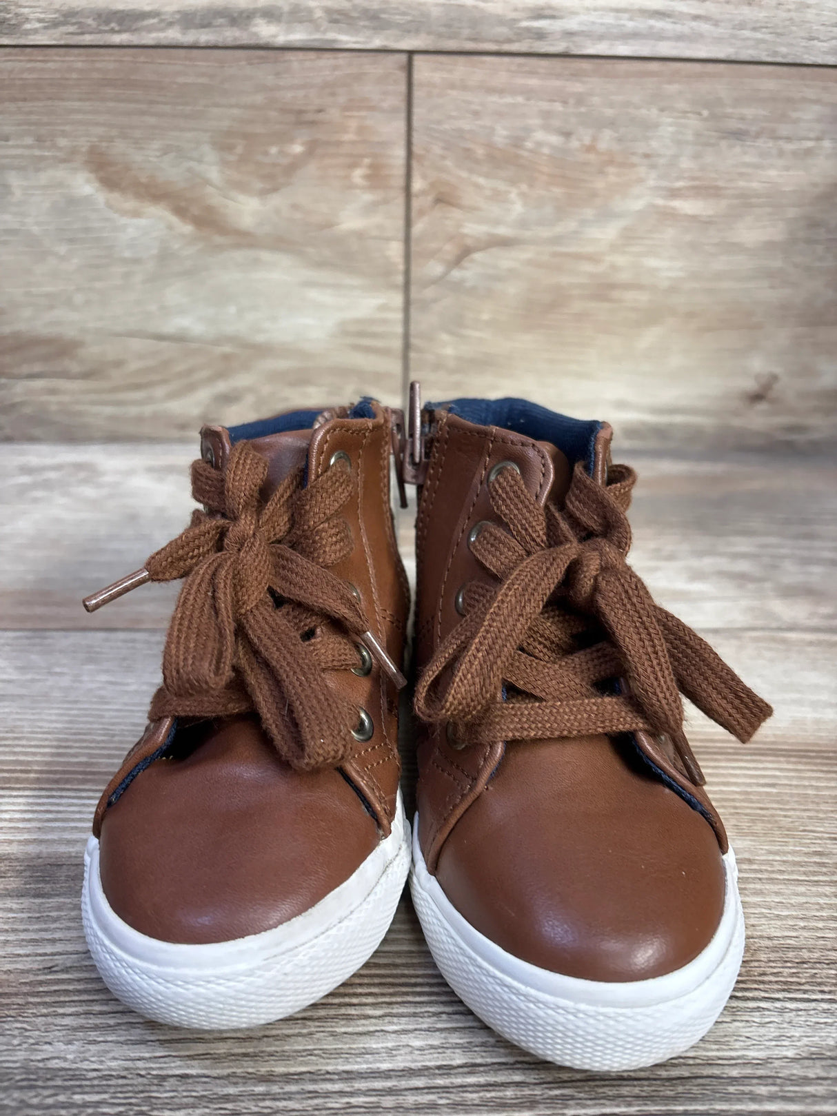 Front view of Cat and Jack Mateo toddler high-top sneakers in brown showing tied laces, side zipper, and white rubber soles on wood background
