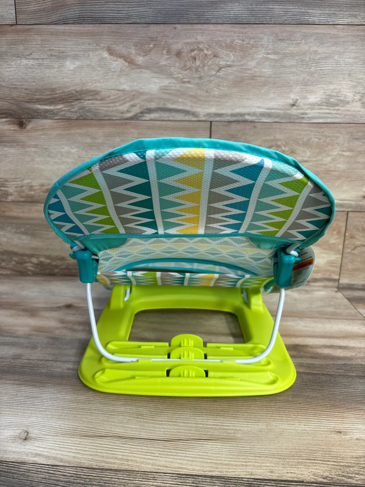 Colorful baby bouncer seat with zigzag pattern and green base on wood floor