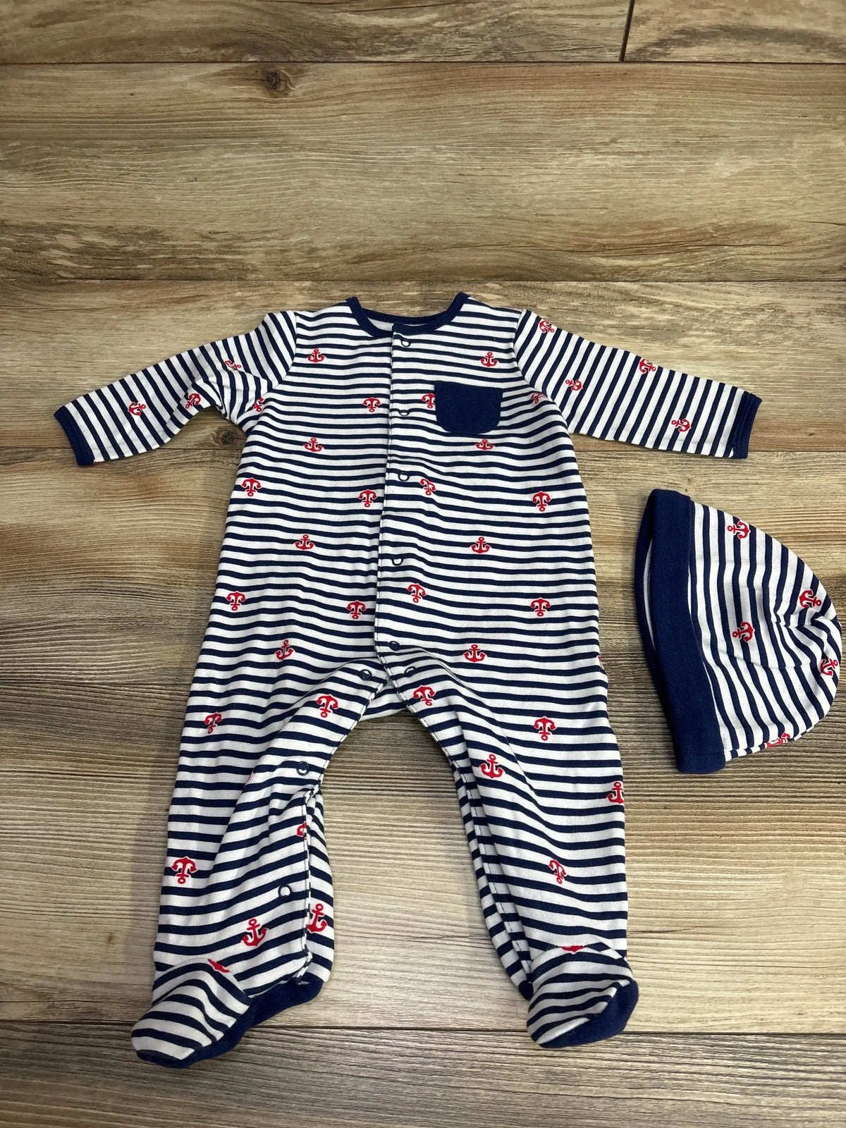 Navy and white striped baby onesie with red anchor prints and matching hat on wooden floor