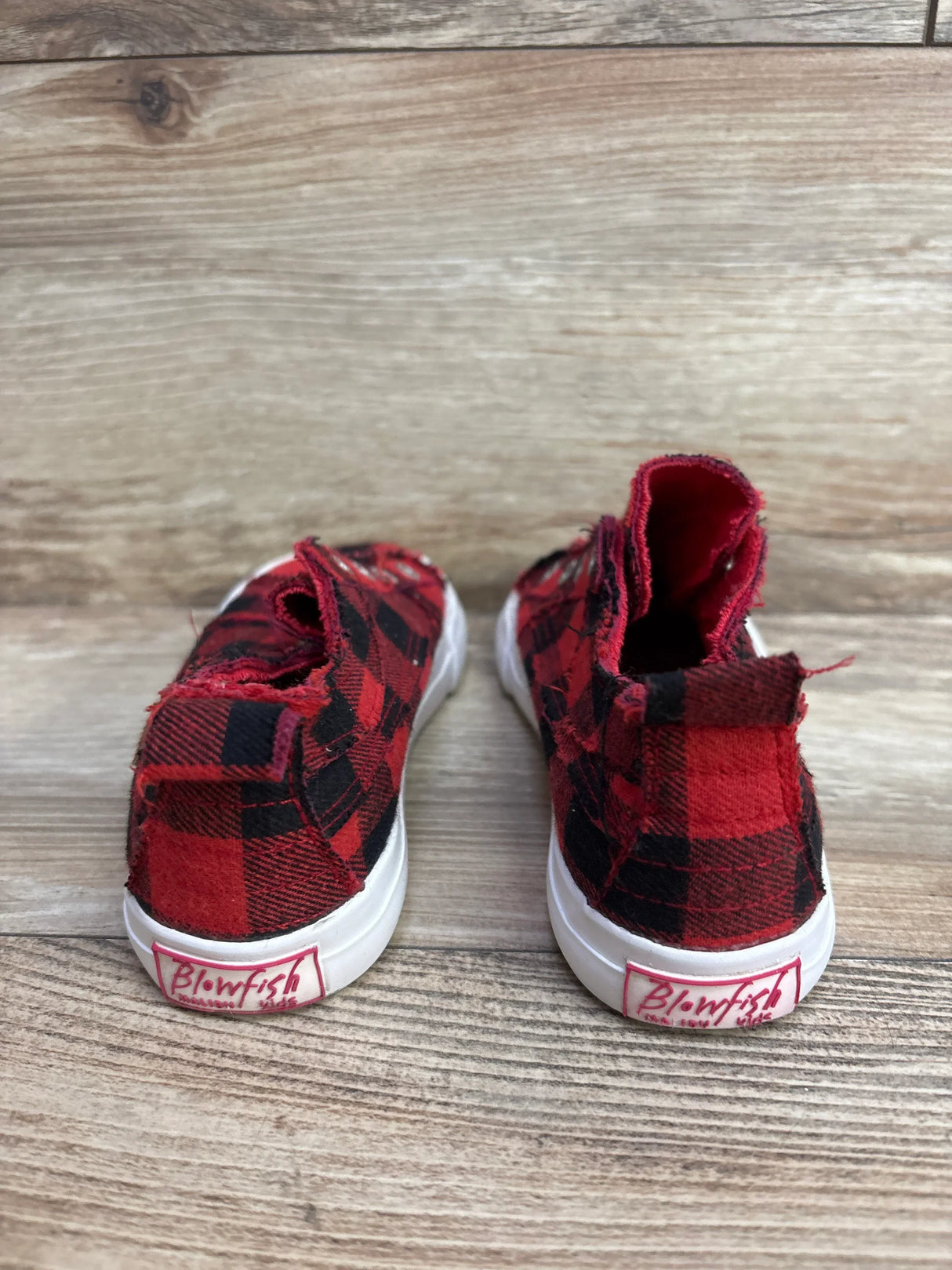 Back view of red and black plaid toddler shoes with white soles on wood surface, Blowfish brand
