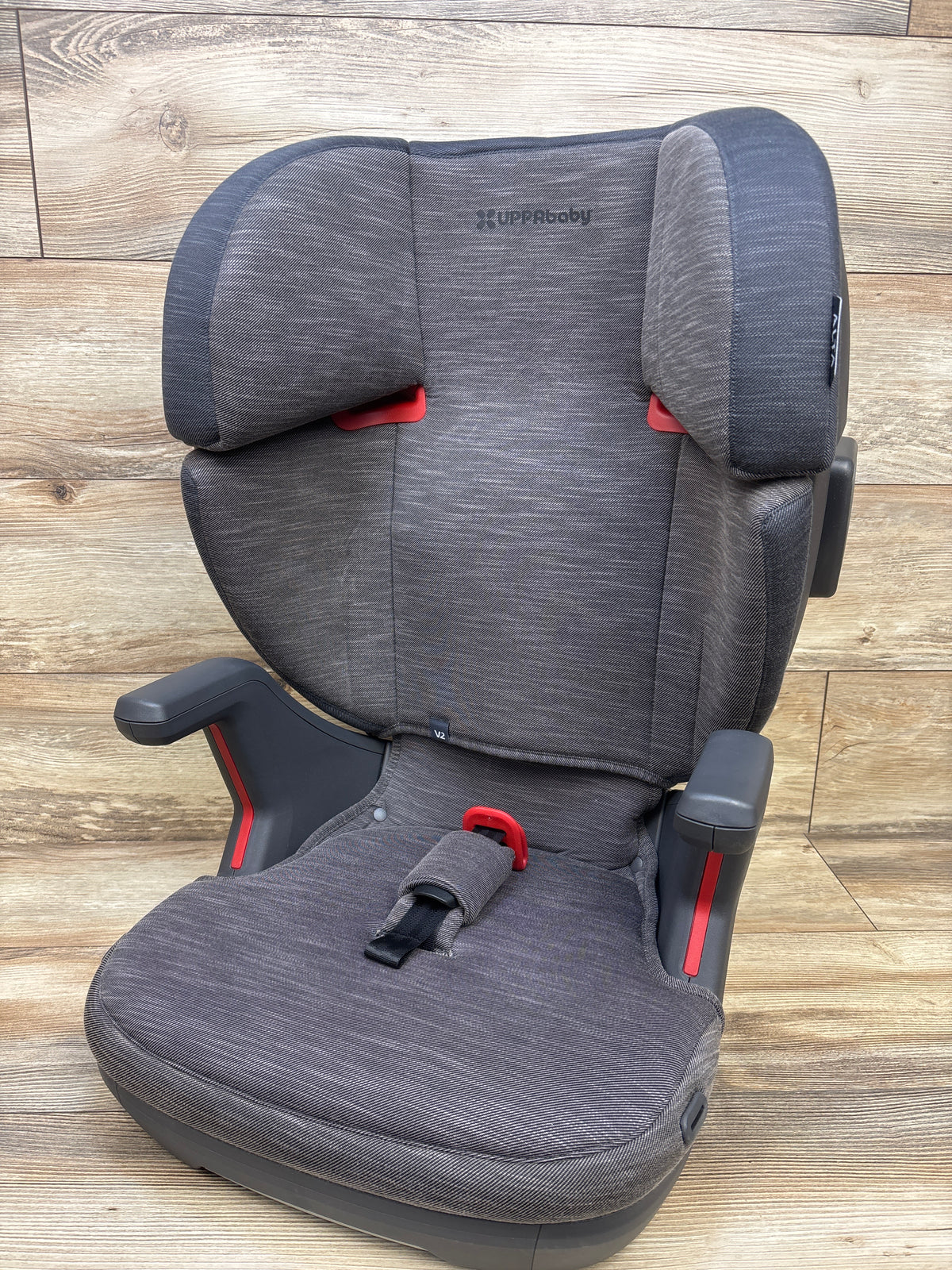 Front view of UPPAbaby Alta V2 High Back Booster Car Seat in Greyson showcasing padded armrests on wood plank background