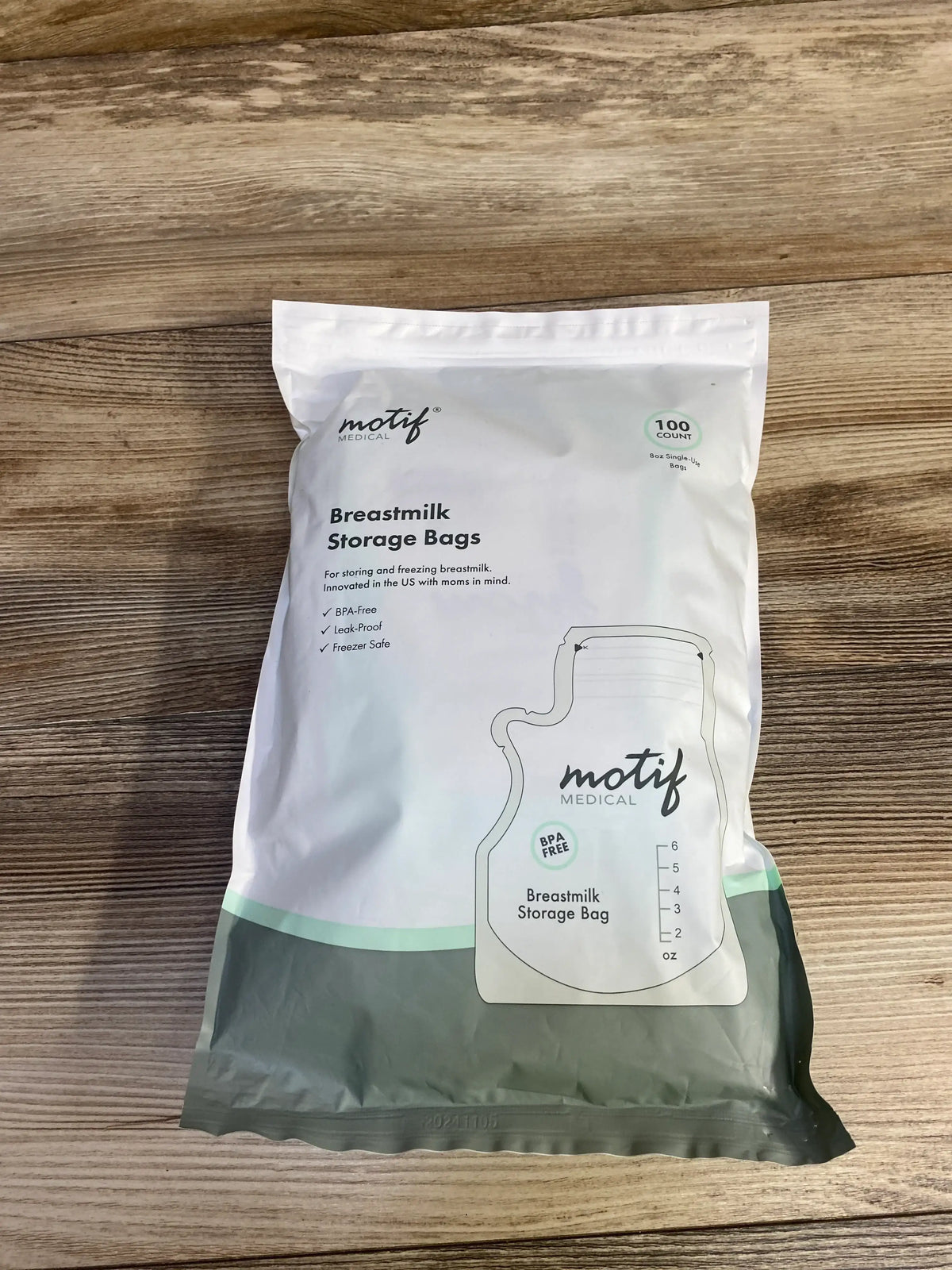 Front view of Motif Medical 100-count breastmilk storage bags pack showing resealable top and measurement markings on wood