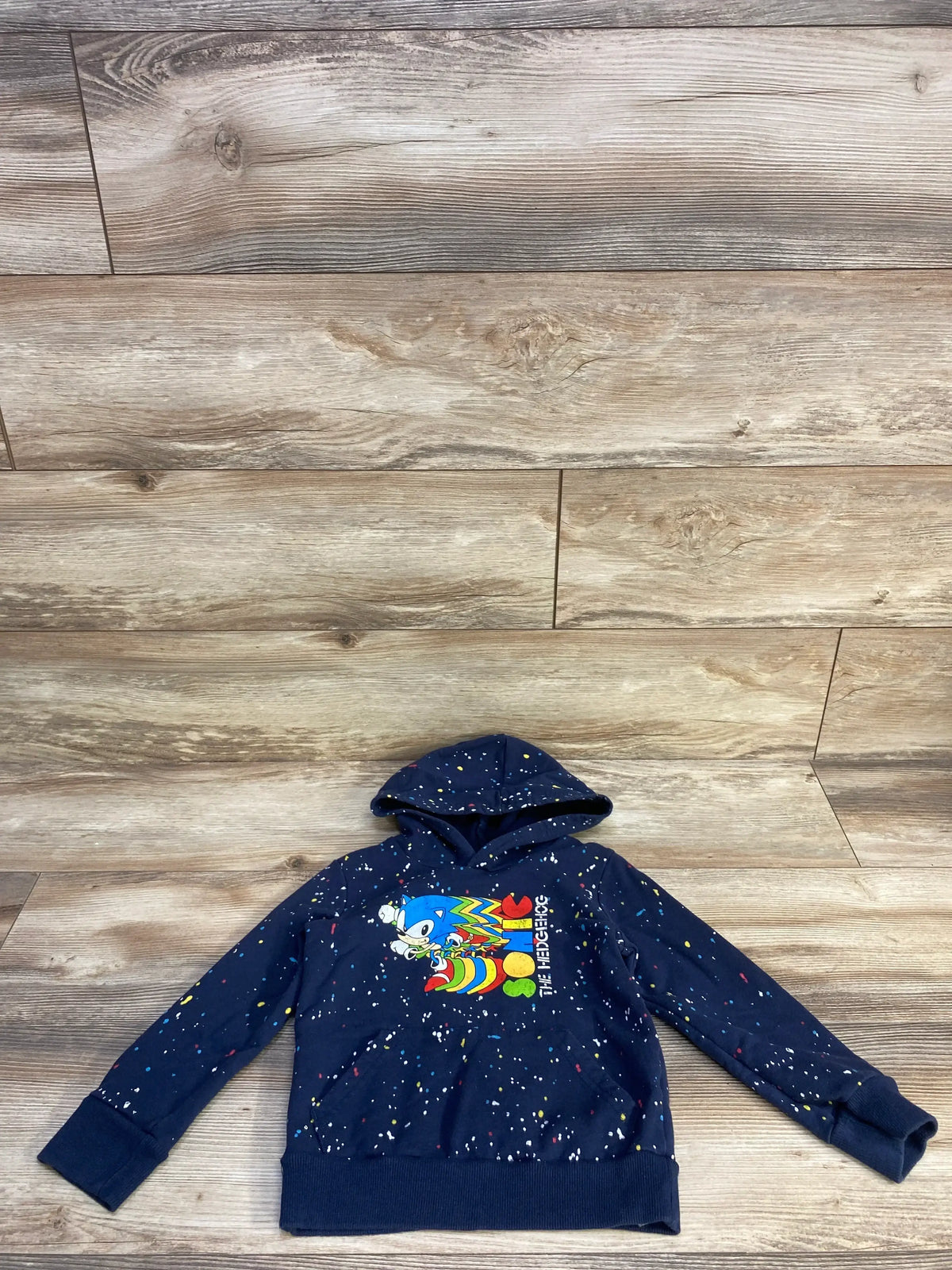 Front of navy Jumping Beans Sonic hoodie showing confetti speckle and rainbow Sonic graphic on wood background