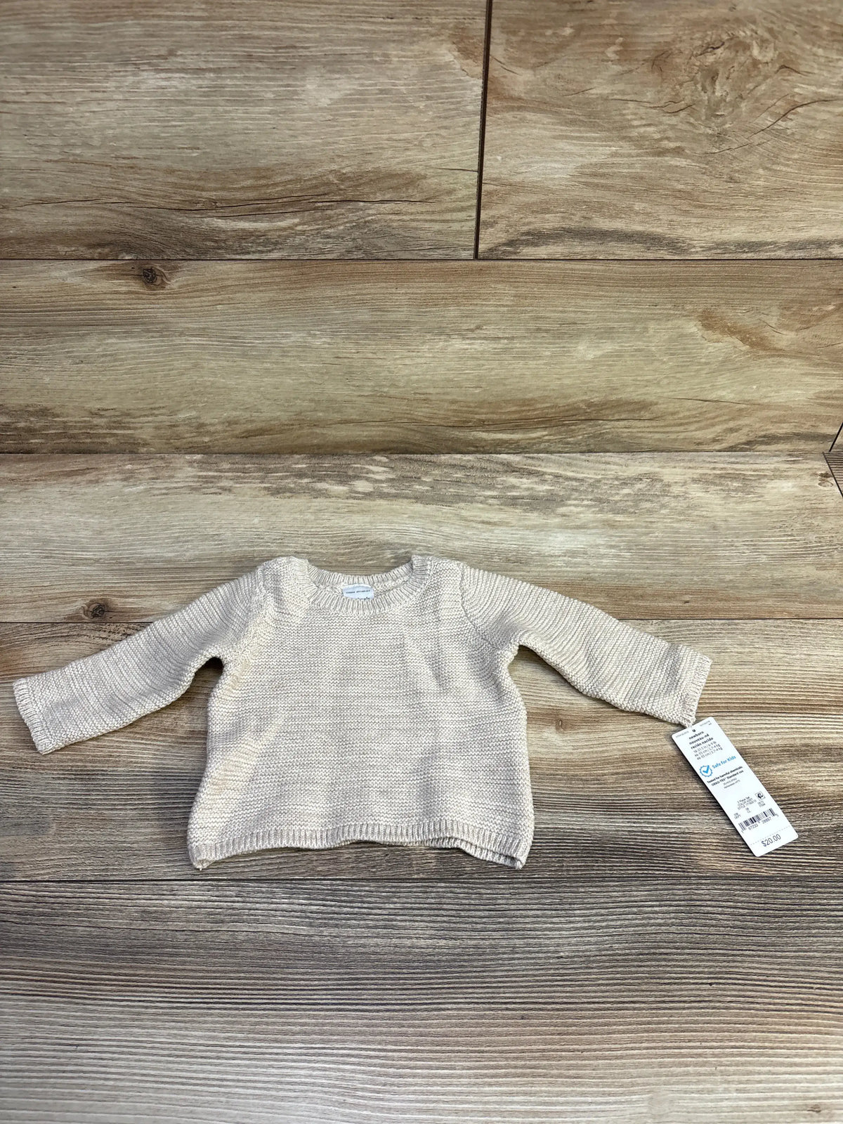 Front flat lay of newborn beige knit sweater showing long sleeves, ribbed hem and knit texture on wooden background