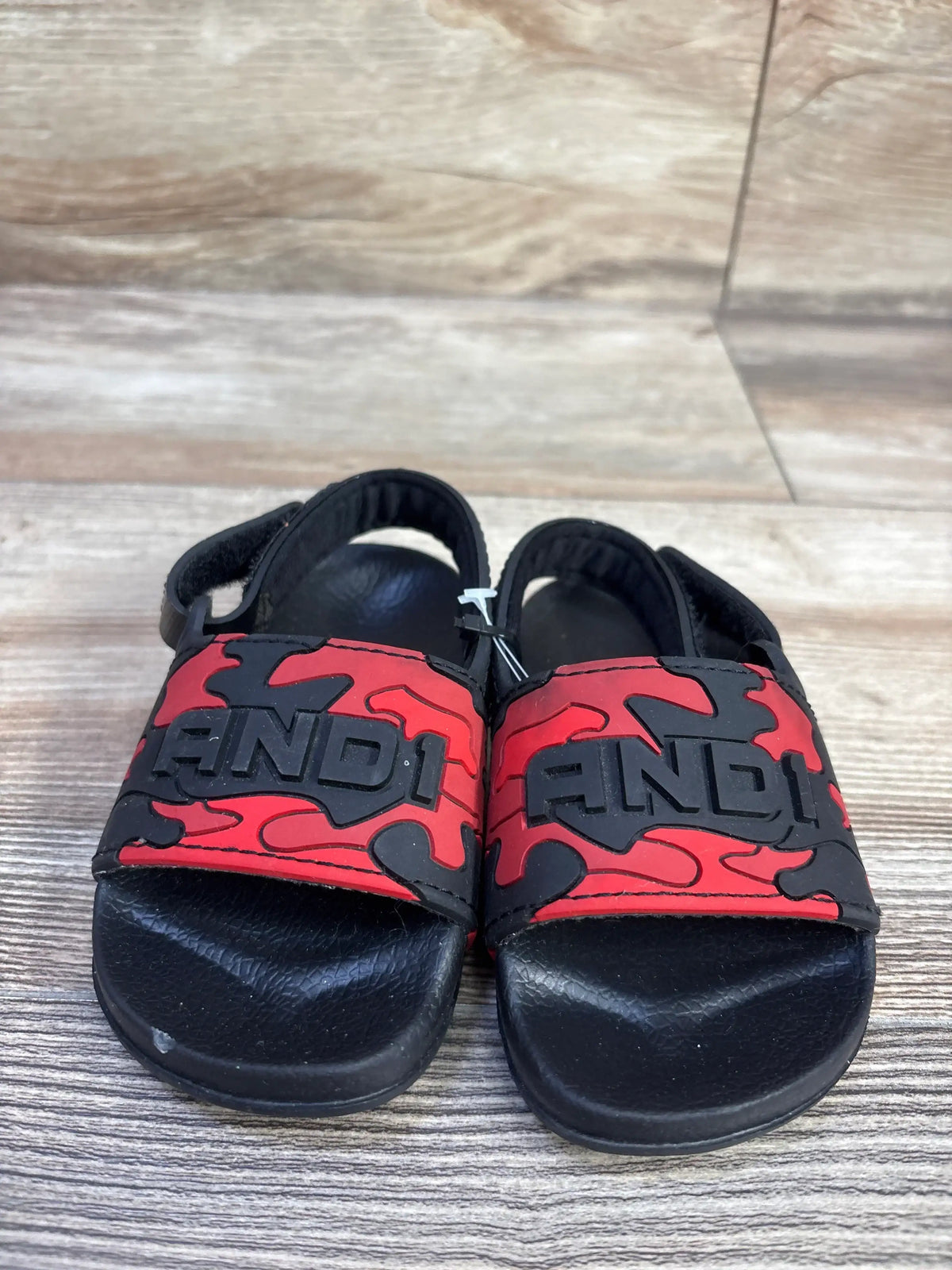 Front view of NWOT And1 Camo Slide Sandals in red and black camo print with logo strap and ankle strap sz 5-6c on wood plank floor