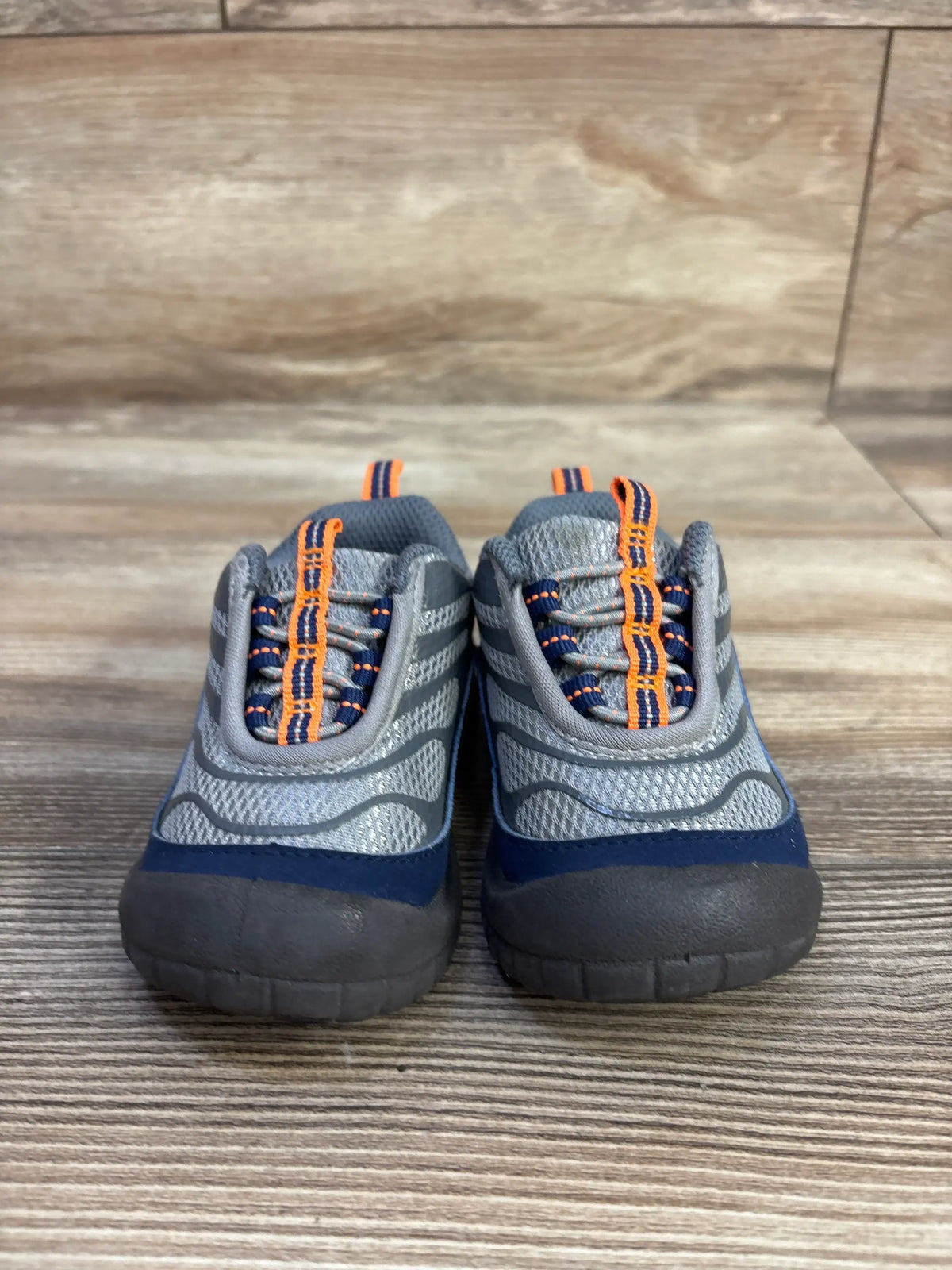 Front view of Oshkosh Gianni bump toe sneakers showcasing reinforced toe protection and orange and navy accents on a wood-look floor
