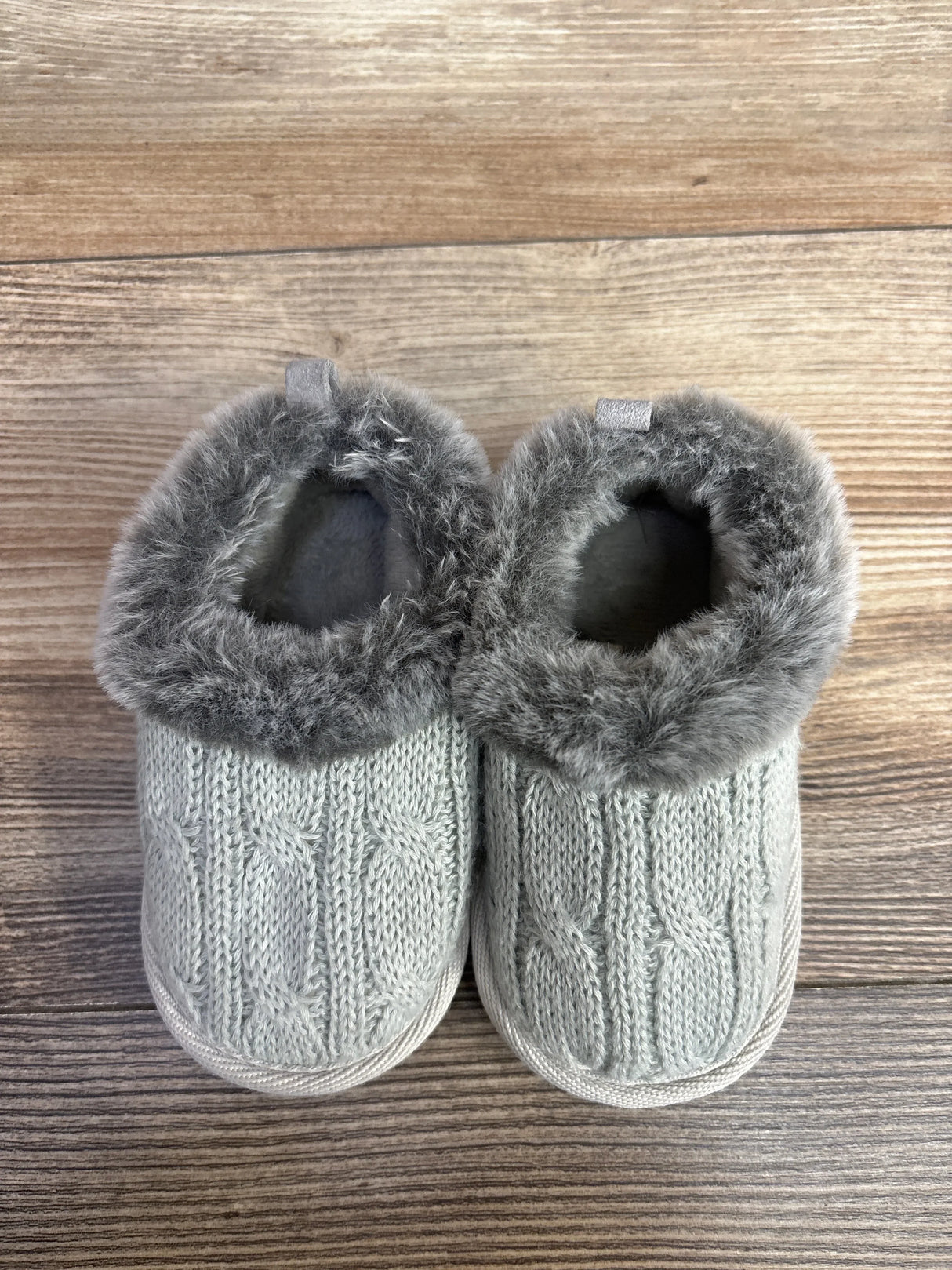 Gray knit baby booties with faux fur trim on wood background