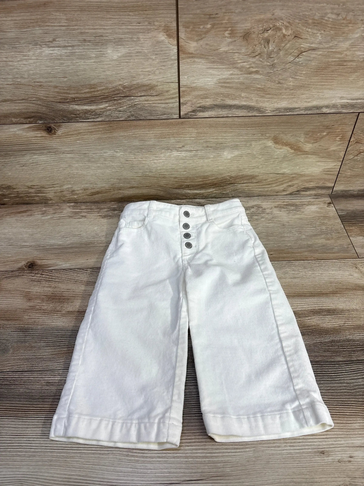 Front view of white toddler corduroy wide-leg pants (18–24 months) showing four-button fly and cuffed hems on wood background