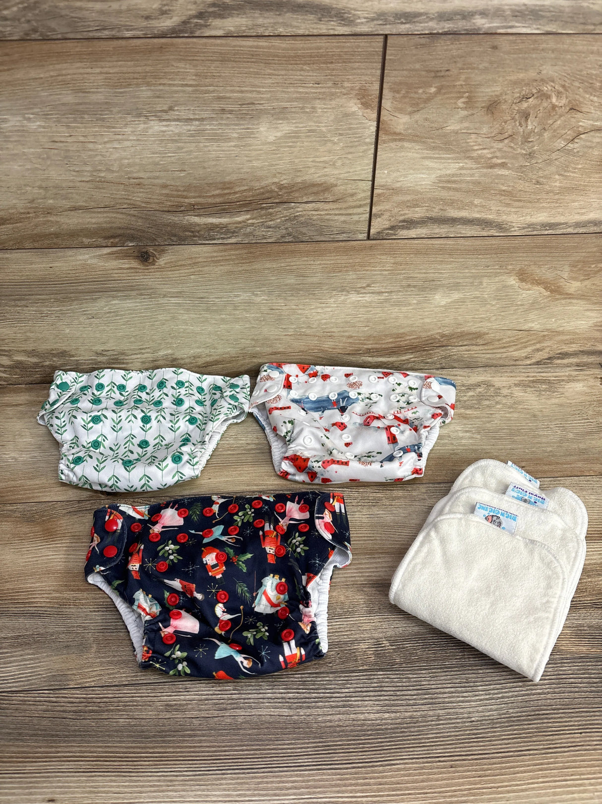 Assorted reusable cloth diapers with colorful prints and inserts on wood floor