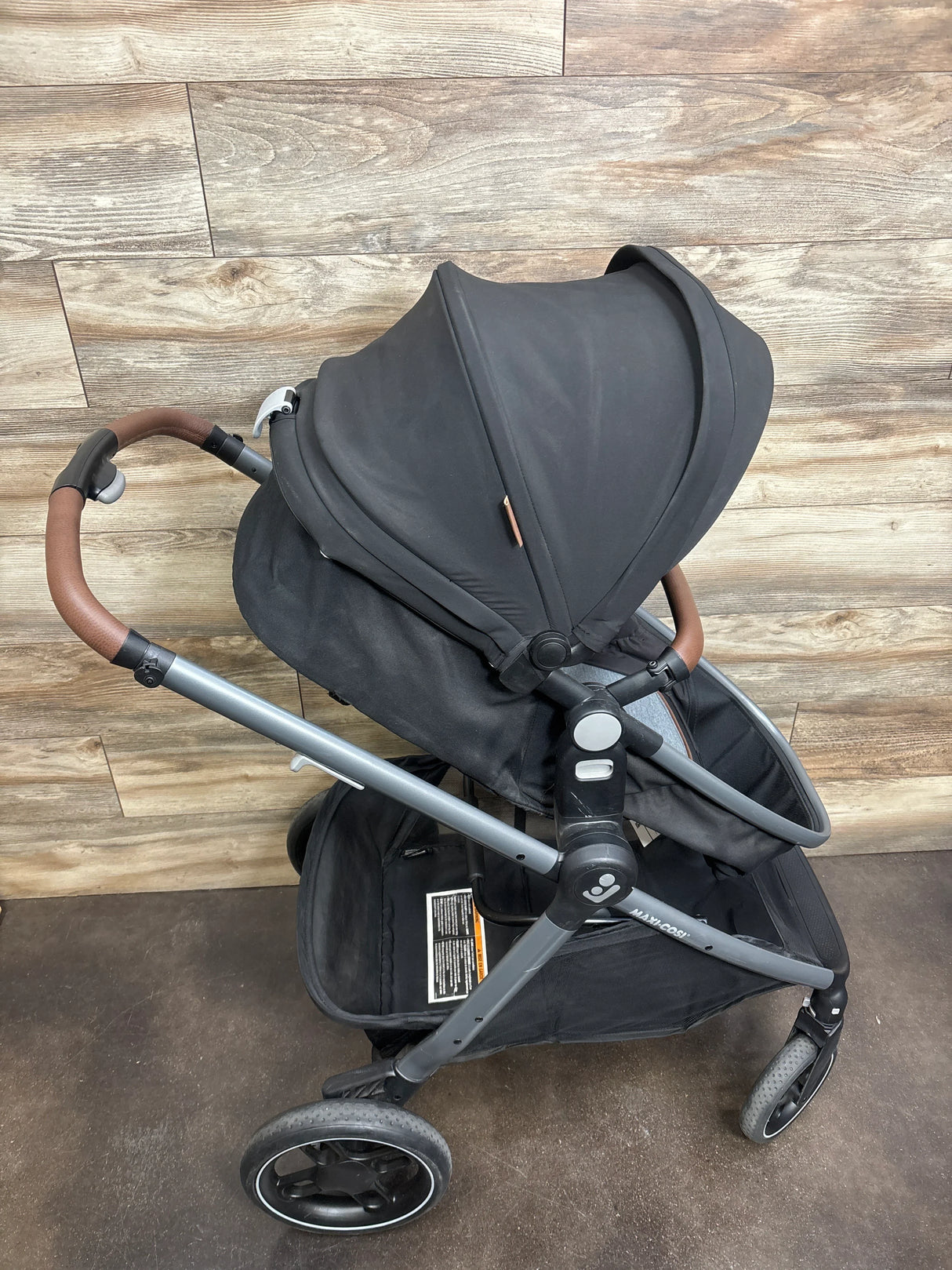 Black baby stroller with brown handles and storage basket, modern wood floor background
