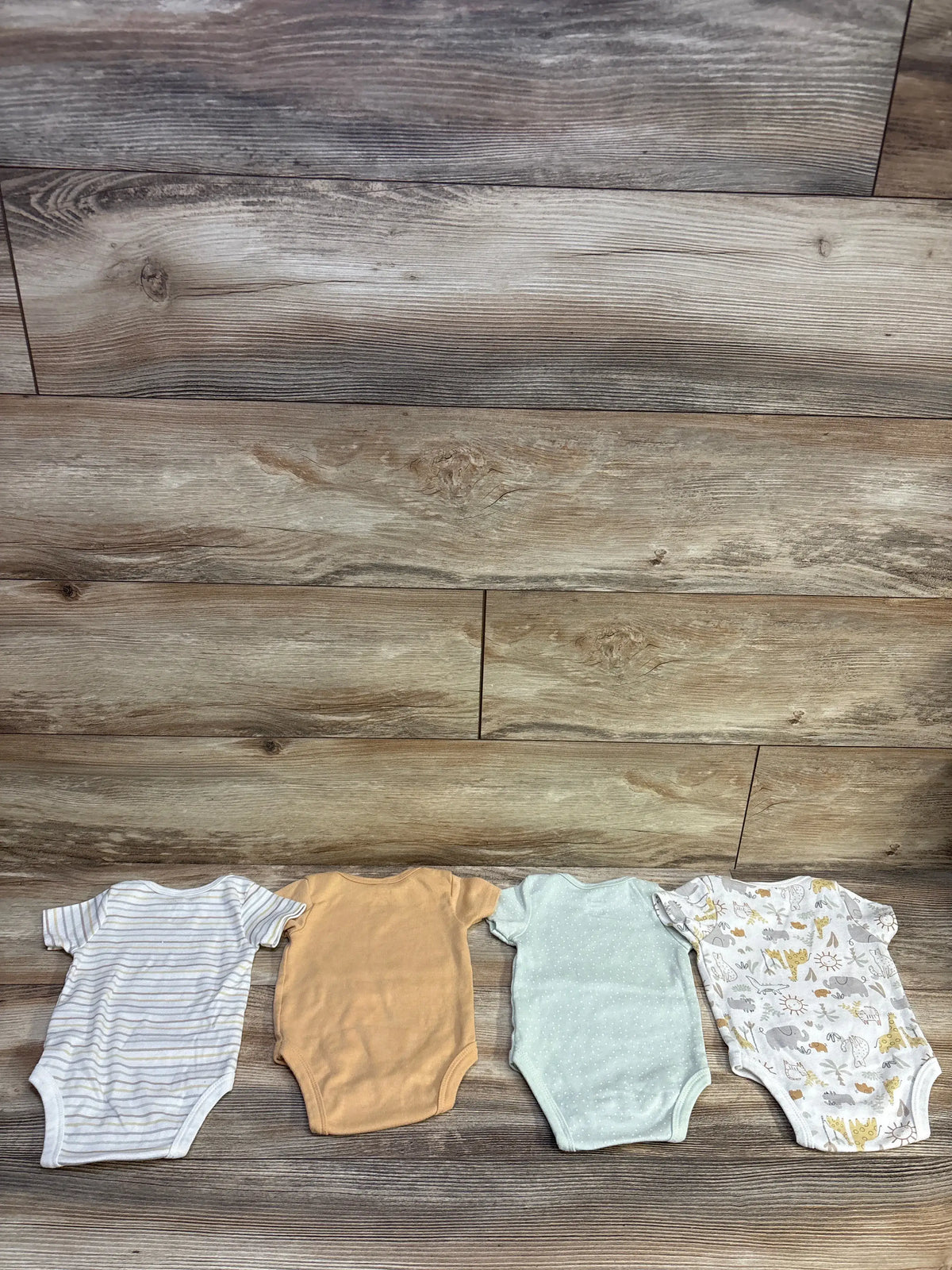 Top view of DreamGro 4-pack bodysuits in striped, tan, mint, and animal prints on a wood-grain background