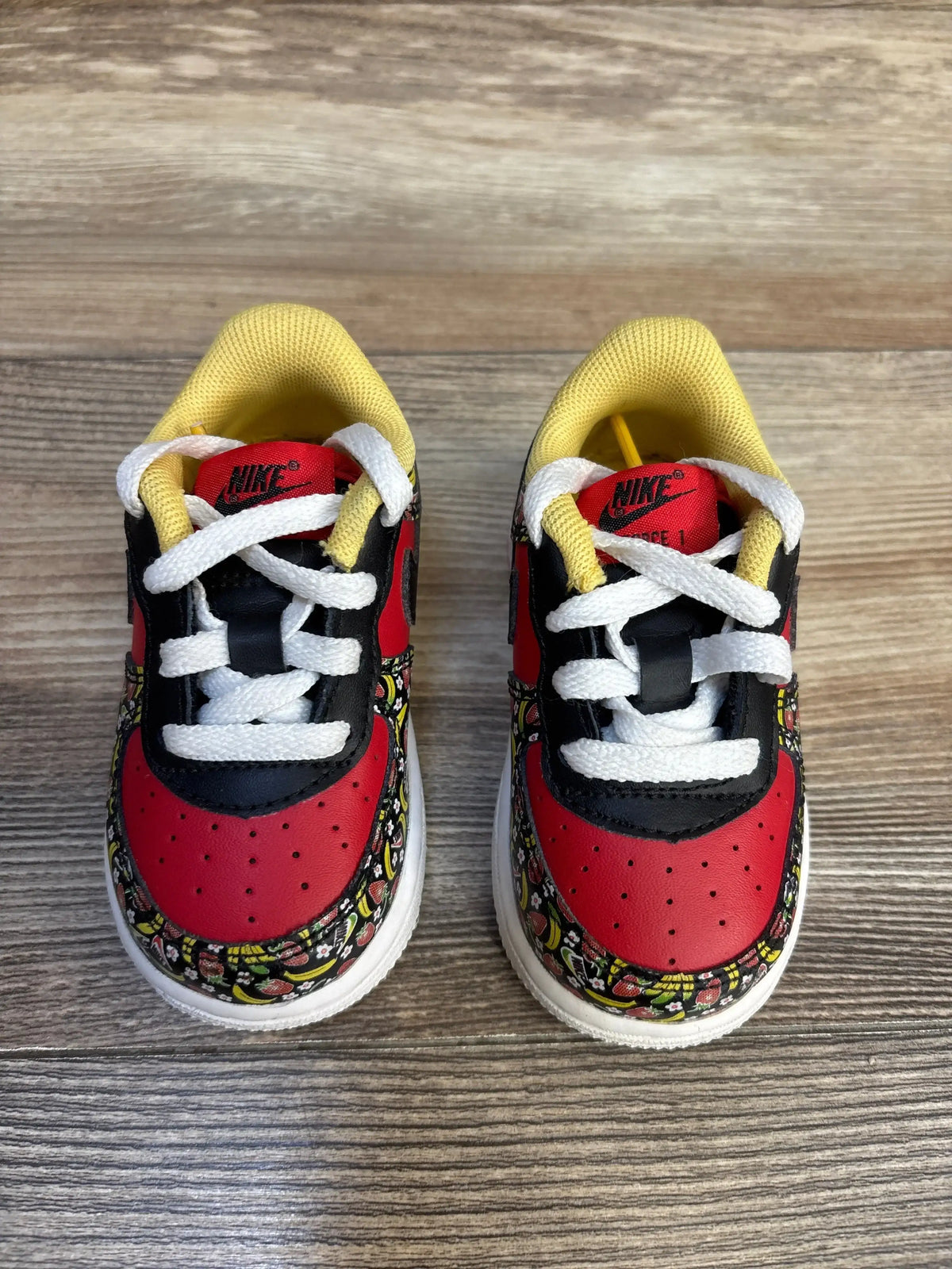 Nike Air Force 1 toddler sneakers with red, black, yellow, and fruit print design on wood floor