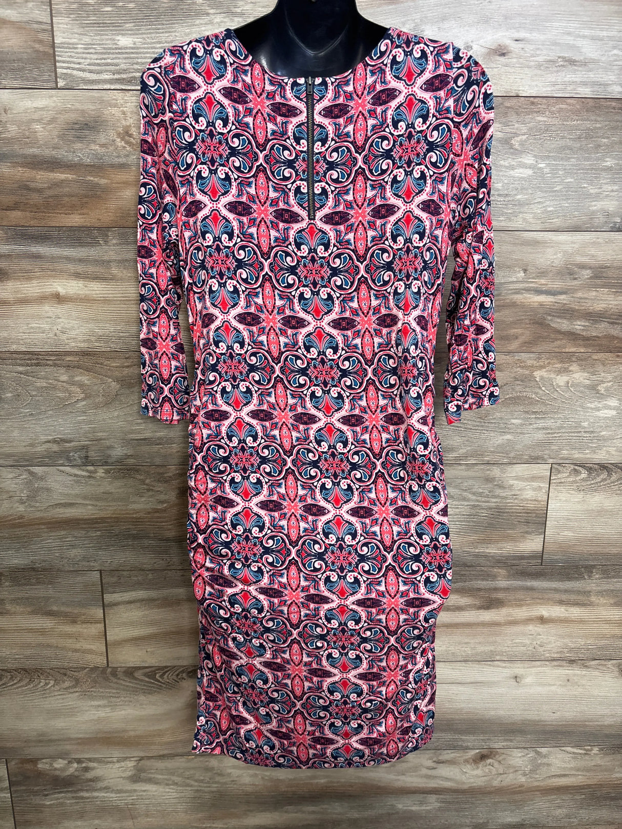 Front view of Jessica Simpson maternity dress showcasing pink and navy medallion print, front zipper and side ruching on wood backdrop