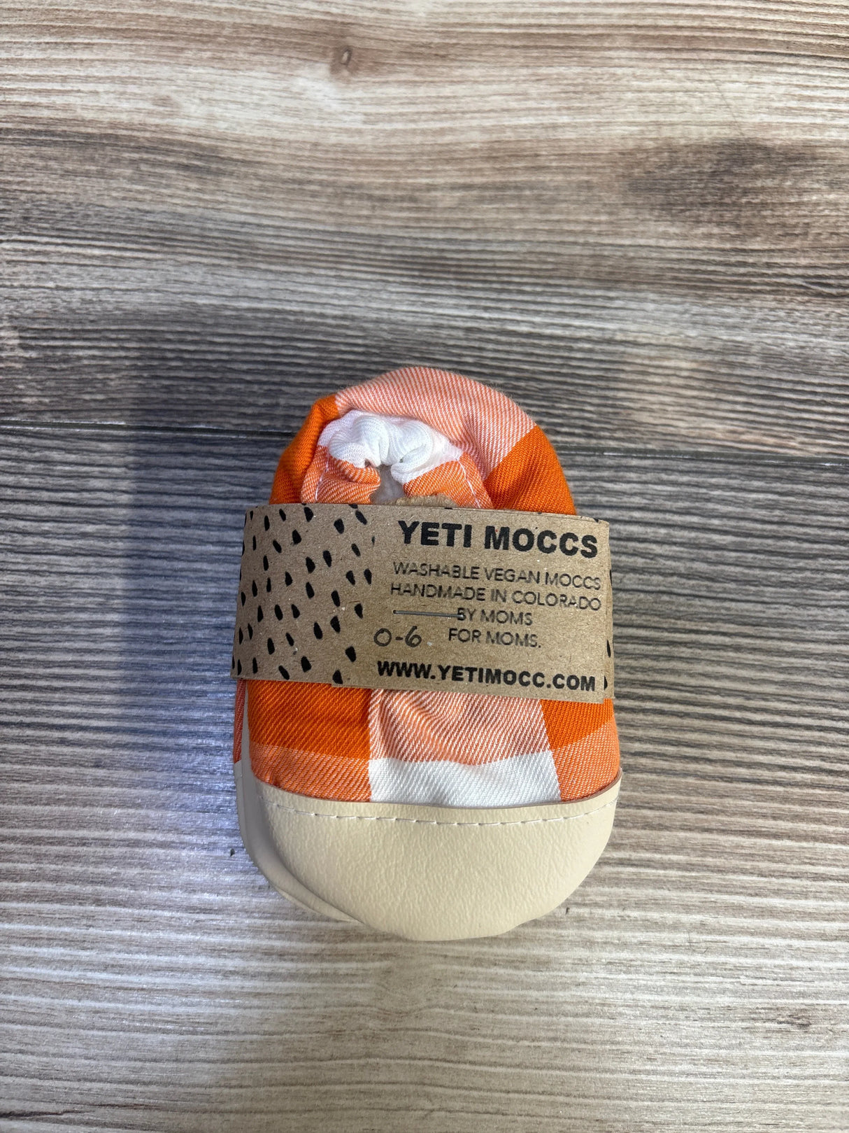 Front view of the Yeti Moccs Classic Mocc orange soft sole shoe showcasing its cream sole on a wood-grain background