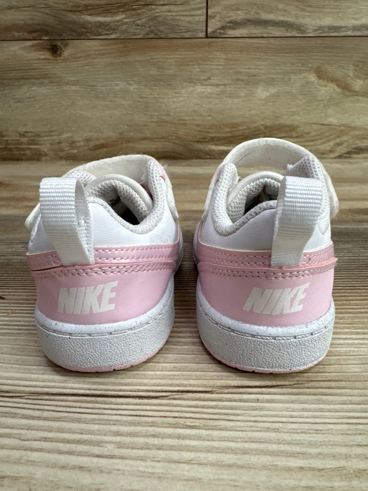 Rear view of Nike Court Borough Low Recraft TD sneakers in Pink Foam White, showing heel branding and pull straps on a wood surface